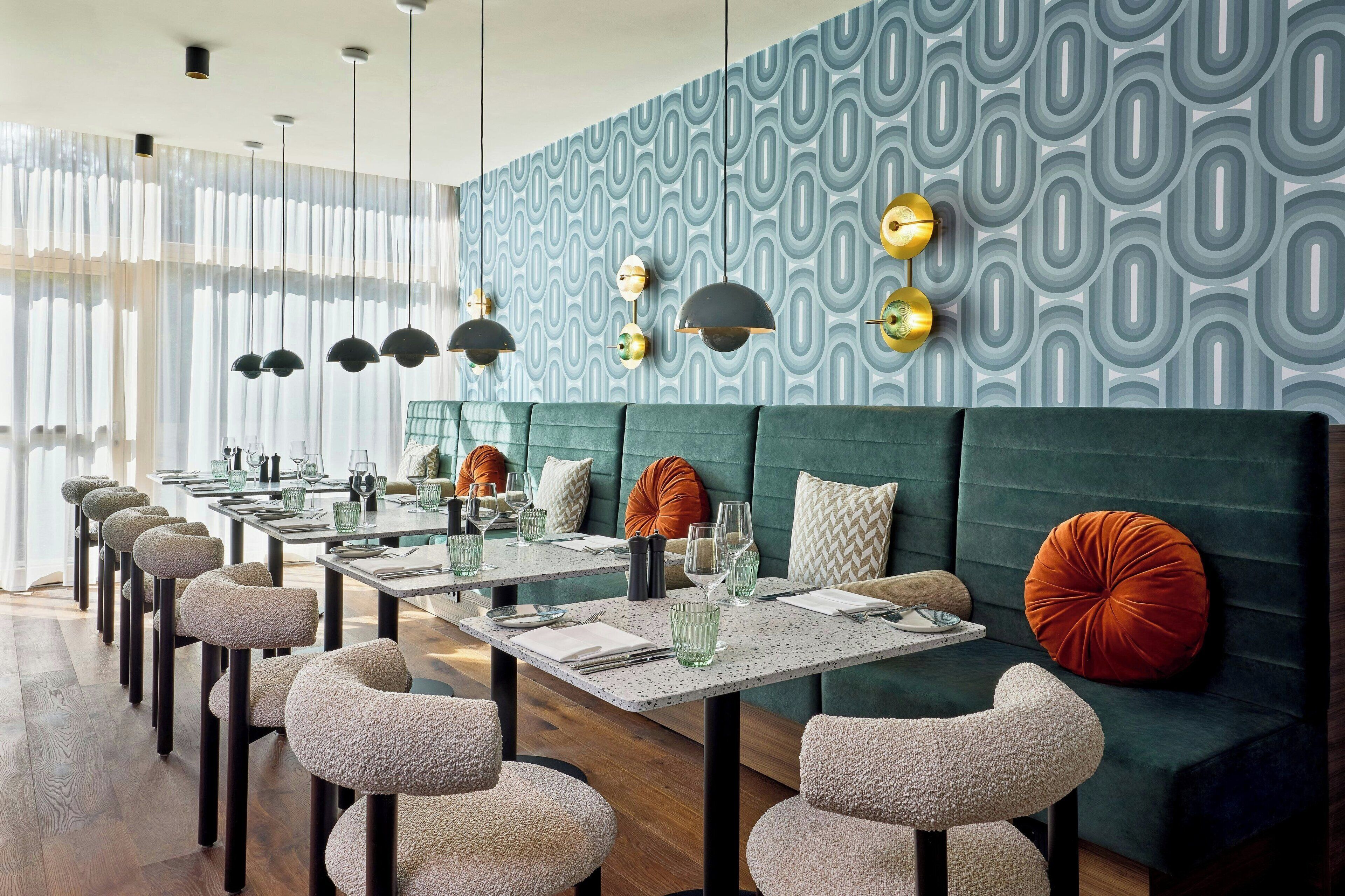 A modern restaurant with a long dining area, green upholstered booths, and a patterned wall.