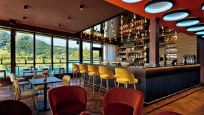 A bar area with a view of mountains, red chairs, and a bar counter with various bottles and glasses. - Flesslers Lenggries, a Tribute Portfolio Hotel (Lenggries)