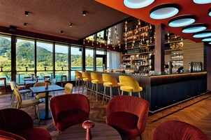A bar area with a view of mountains, red chairs, and a bar counter with various bottles and glasses.