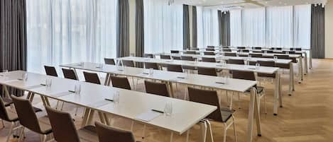 Un salón de conferencias con varias mesas y sillas, ventanas amplias con cortinas y un diseño de techo moderno.