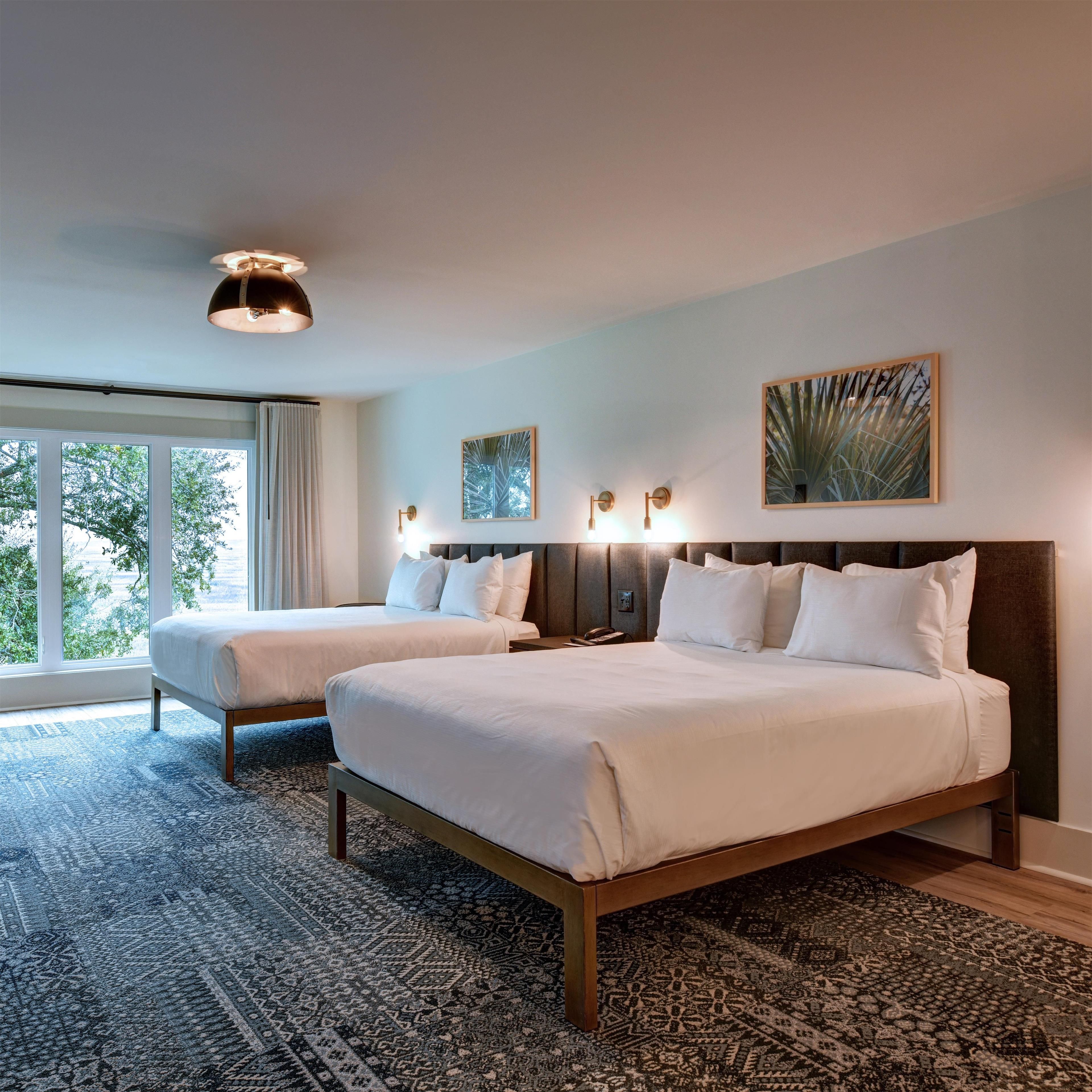 A hotel room with two beds, a large window, and a patterned carpet.