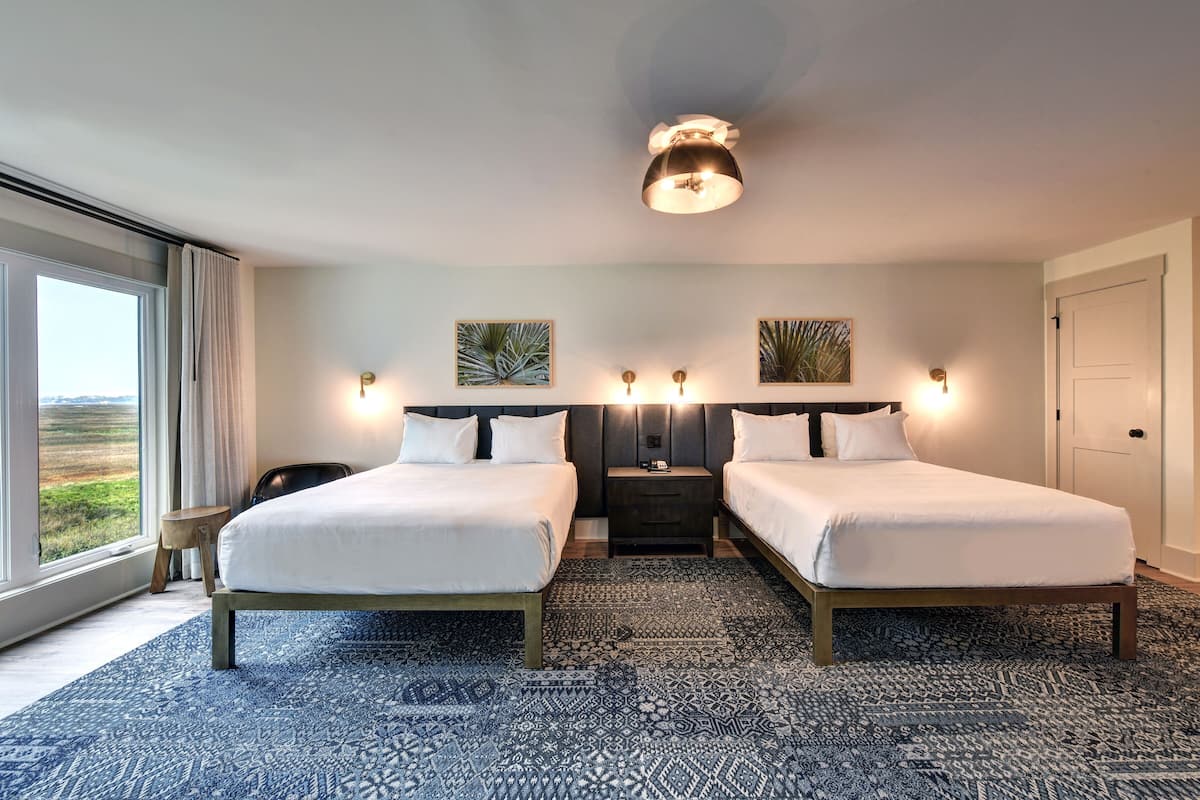 Habitación de hotel con dos camas, un ventanal con vistas y una alfombra estampada.