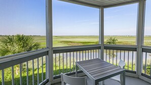 A covered outdoor area with a table and chairs, overlooking a grassy field and a body of water. - Sea Palms Resort St Simons Island (St. Simons Island)