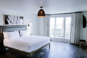 Una camera da letto moderna con un letto grande, una lampada a sospensione, una finestra con tende e un quadro appeso al muro.