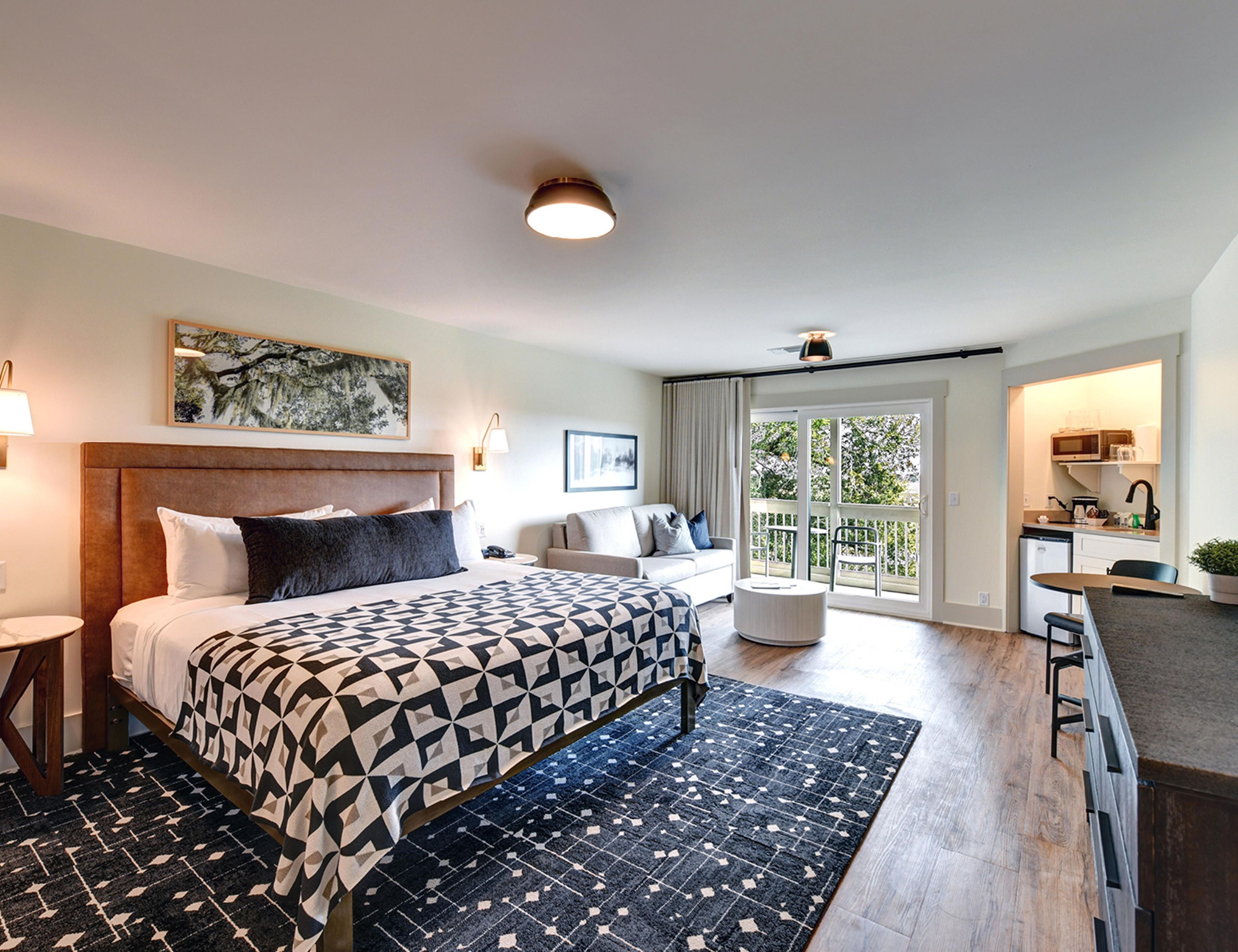 A hotel room with a large bed, a sofa, a dining area, and a balcony with a view.