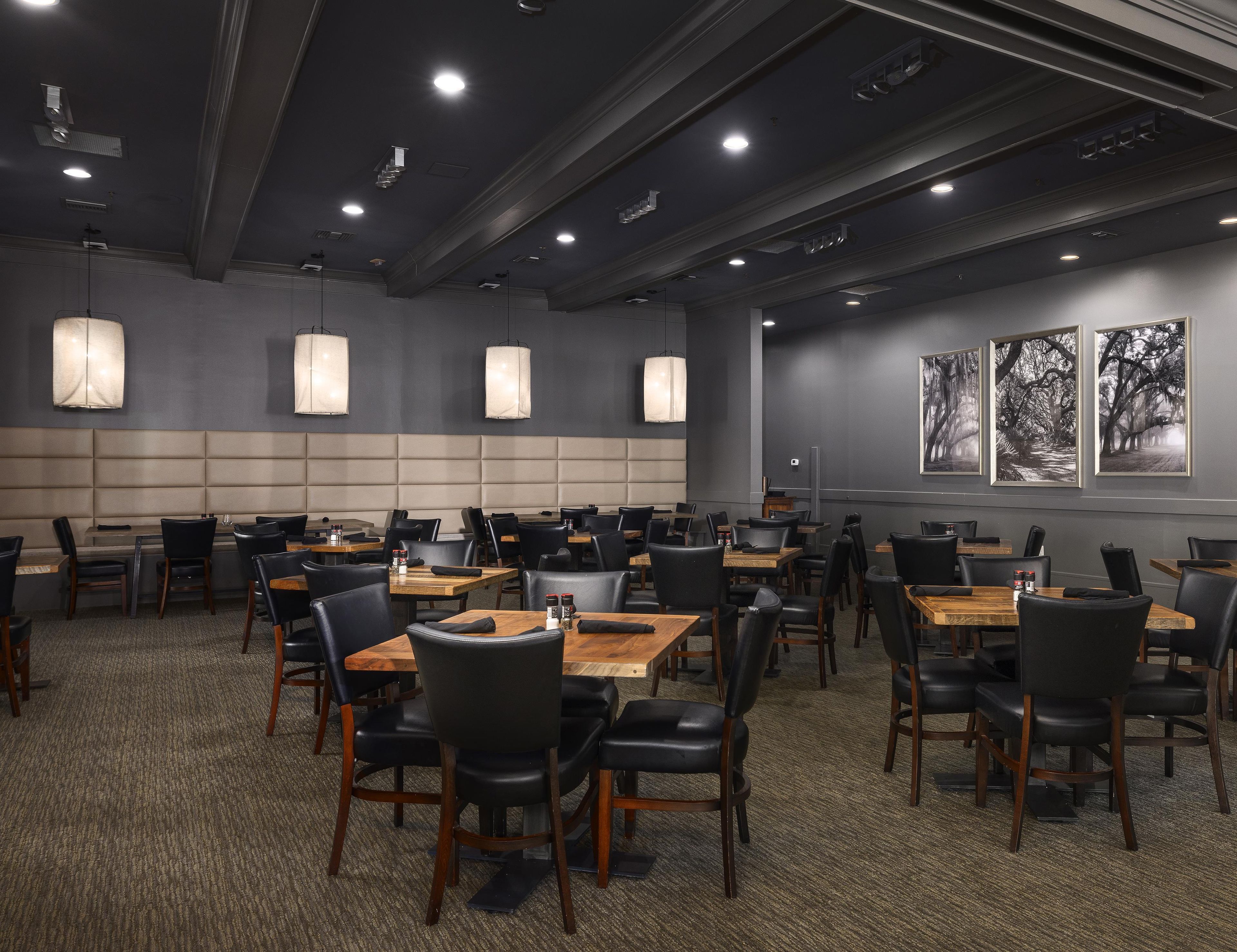 Un ristorante con diversi tavoli e sedie, illuminazione a sospensione e quadri appesi alle pareti.