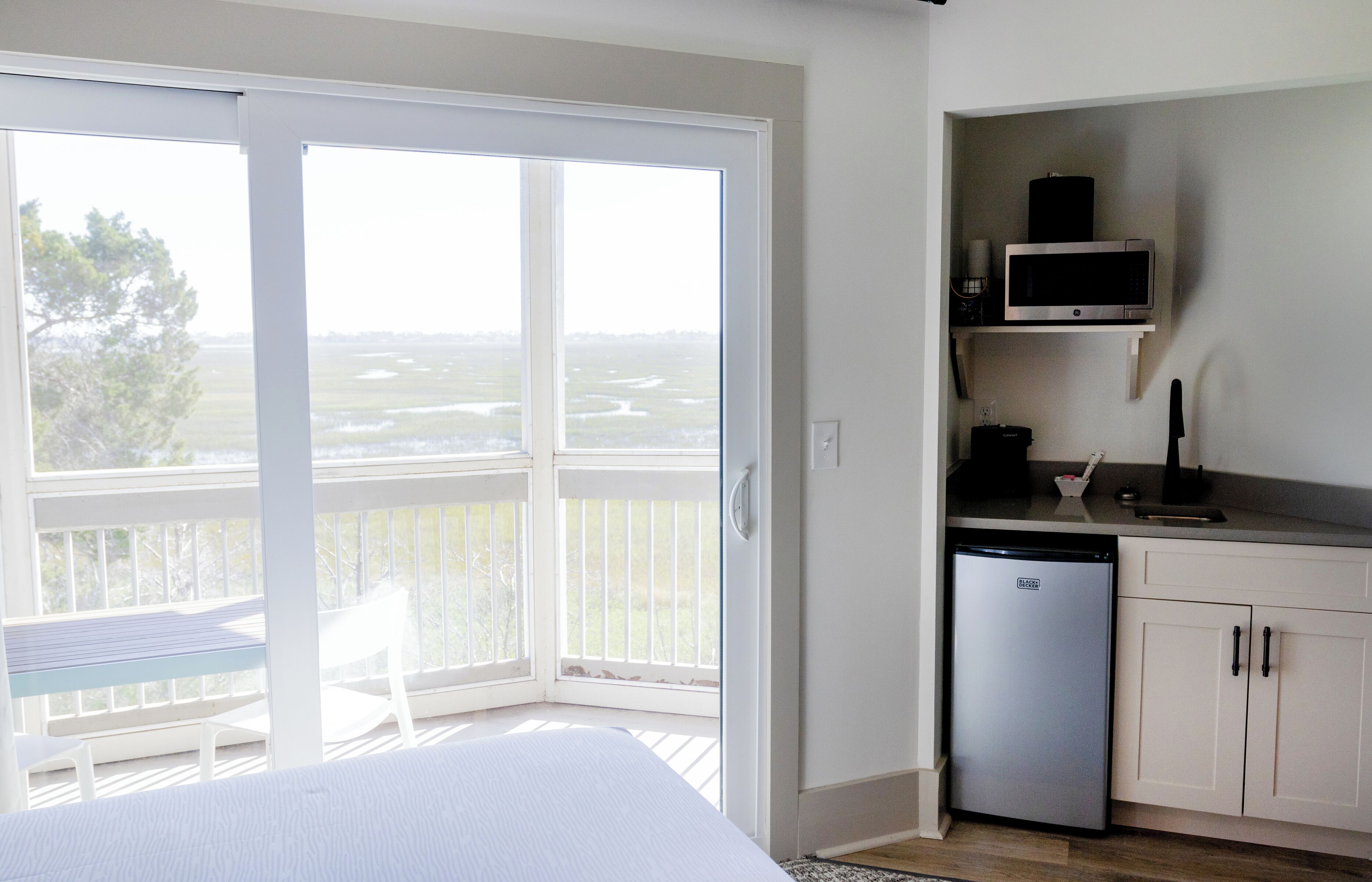 A room with a bed, a small kitchenette, and a sliding glass door leading to a balcony.
