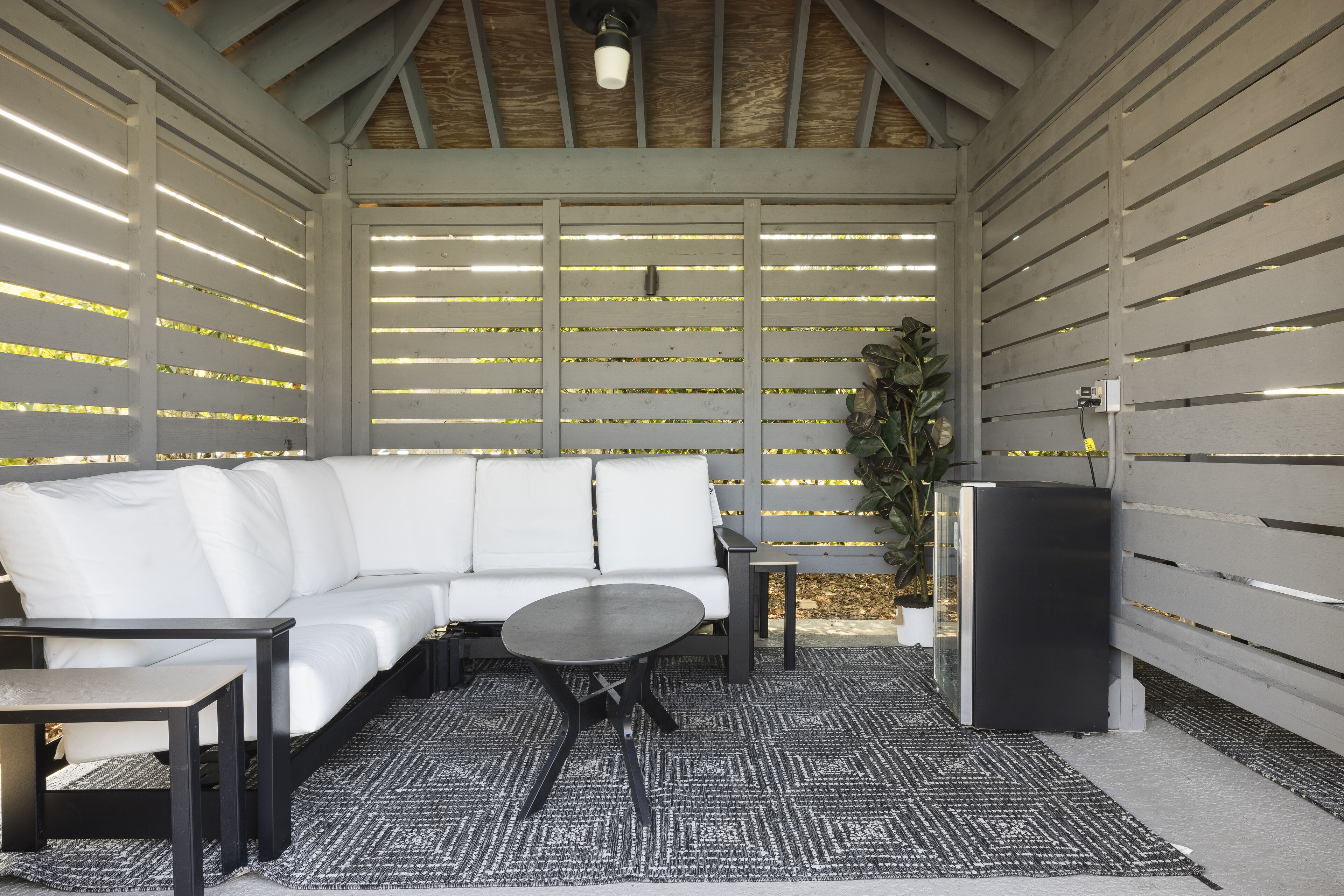 An outdoor patio with a white sofa, a round table, and a small black refrigerator.