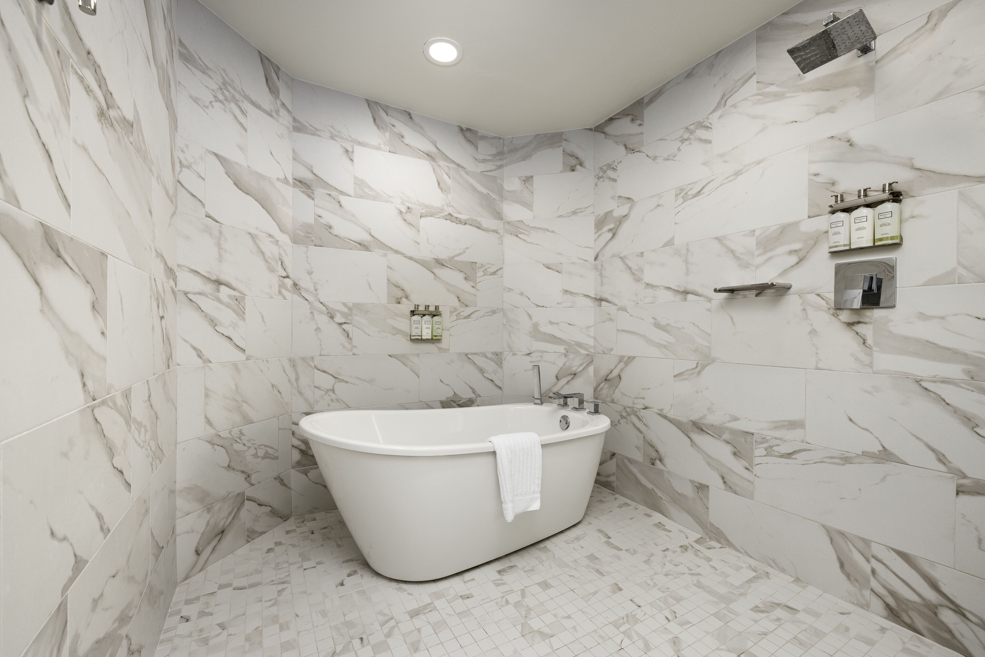 A modern bathroom with a freestanding bathtub, marble walls, and a tiled floor.