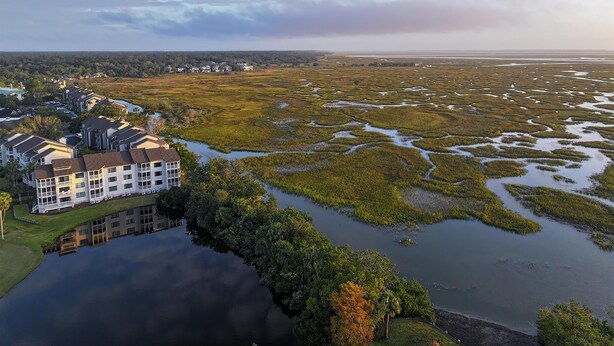 A large building with multiple floors and a waterfront view, surrounded by a marshy landscape. - Sea Palms Resort St Simons Island (St. Simons Island)