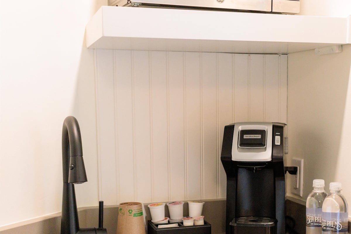 Una cocina con un lavamanos de acero inoxidable, una cafetera y dos botellas de agua sobre la encimera.
