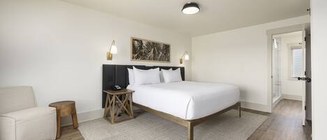 A bedroom with a bed, a bedside table, a chair, and a door leading to another room.