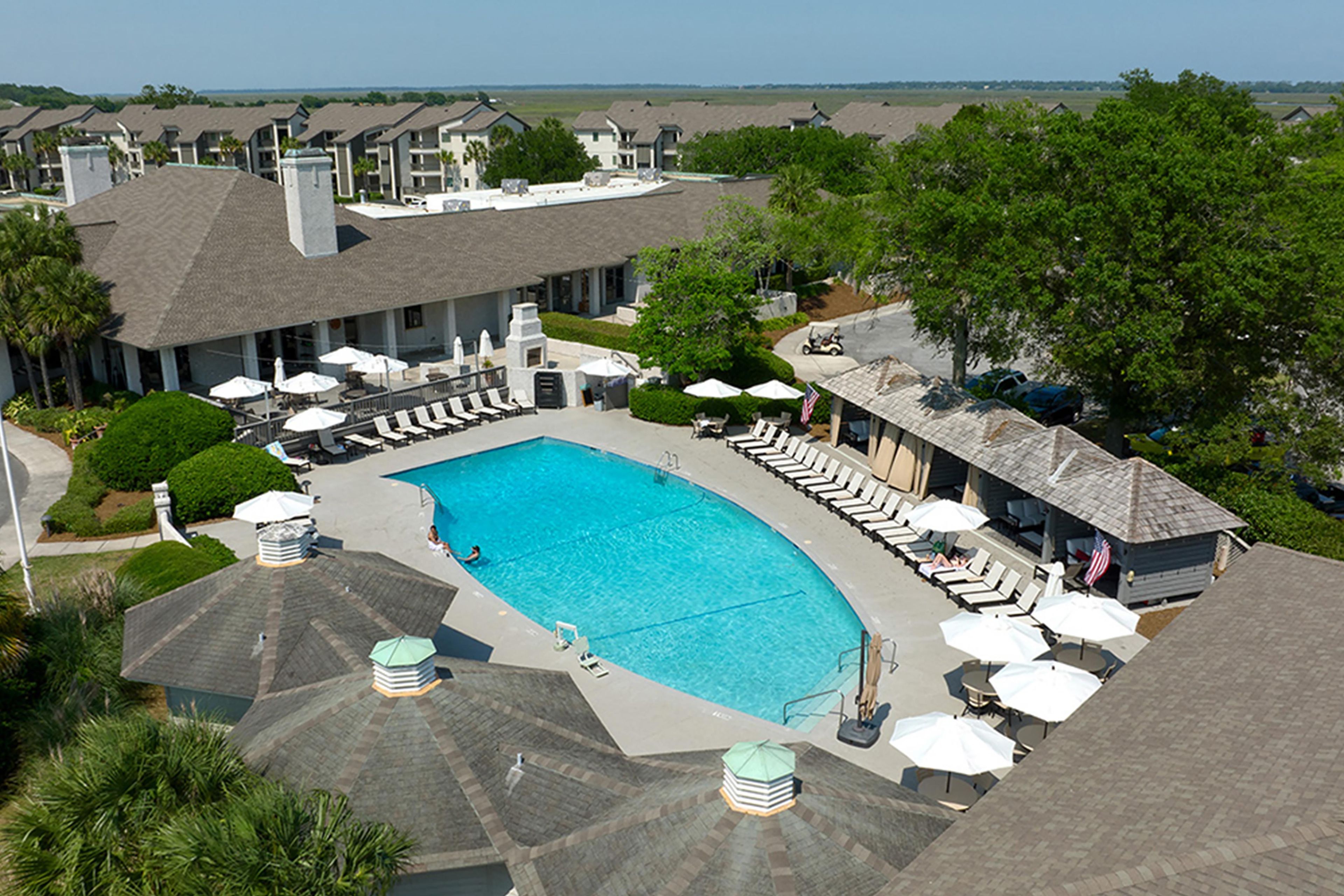 A swimming pool with lounge chairs and umbrellas, surrounded by a building with a covered patio area.
