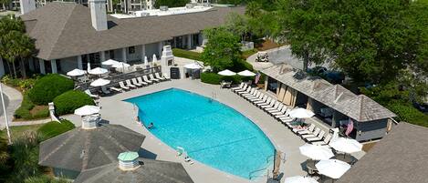 A swimming pool with lounge chairs and umbrellas, surrounded by a building with a covered patio area.