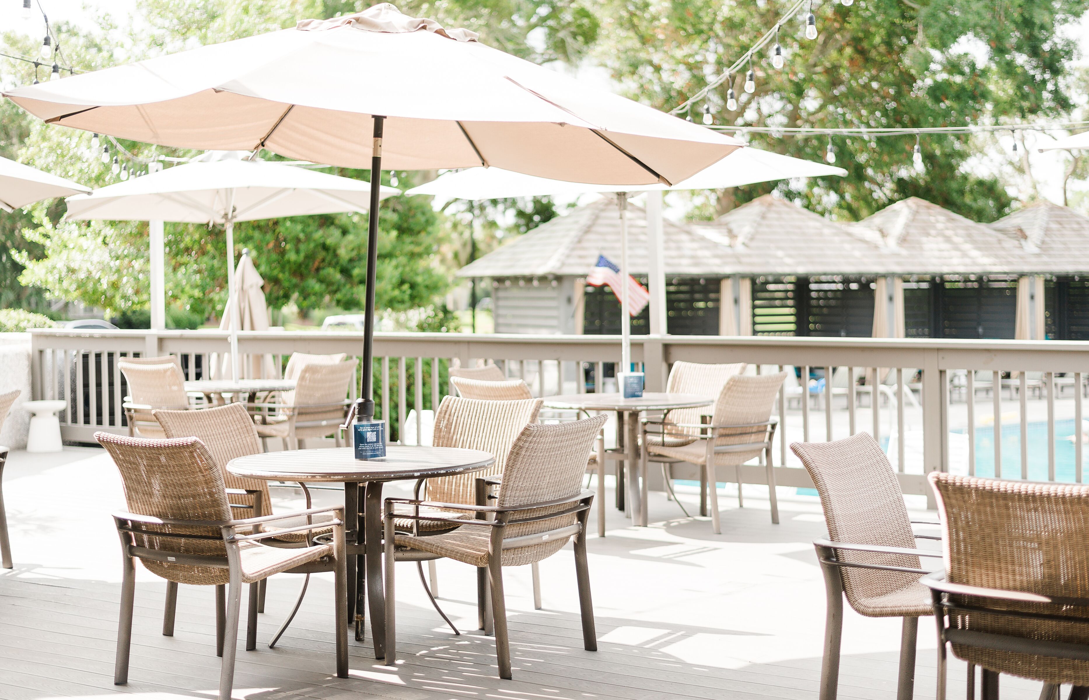 An outdoor patio with wicker furniture and umbrellas, overlooking a pool area.