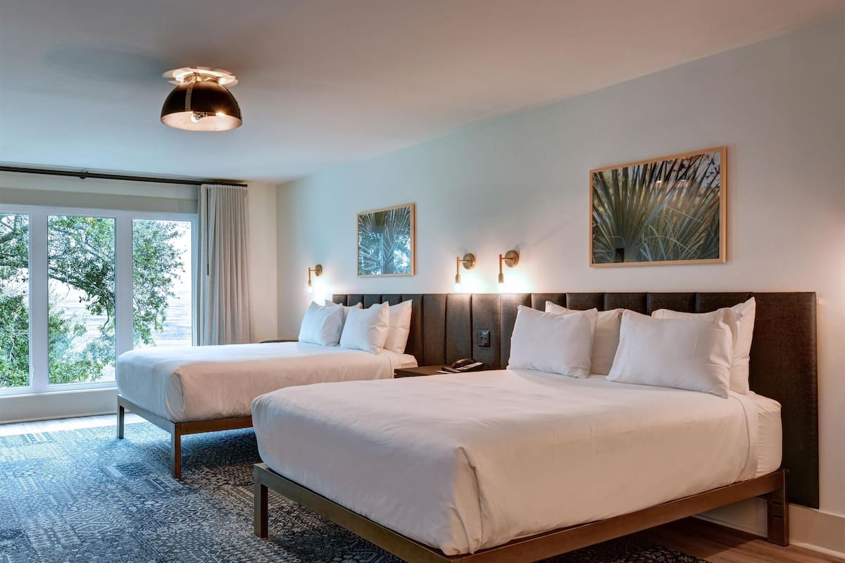 Habitación de hotel con dos camas, un ventanal grande y una alfombra estampada.