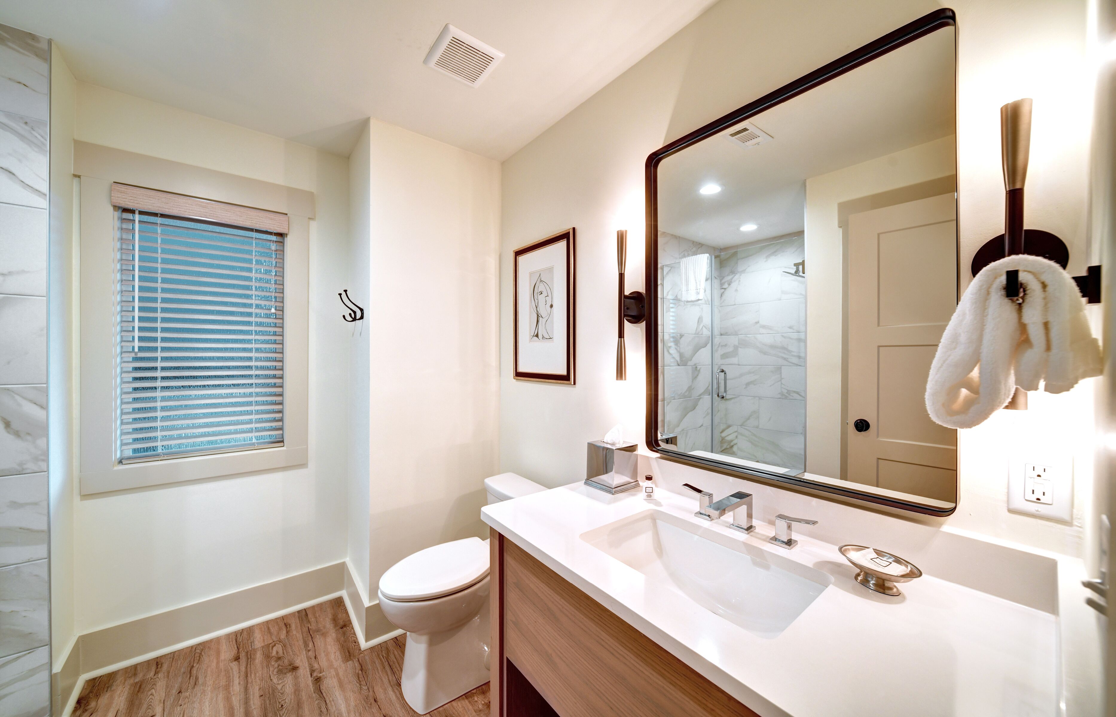 Un baño moderno con un espejo grande, lavamanos blanco y retrete.