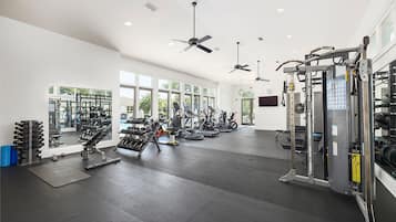 Un gimnasio con ventiladores de techo, equipamiento de ejercicio y amplias ventanas.