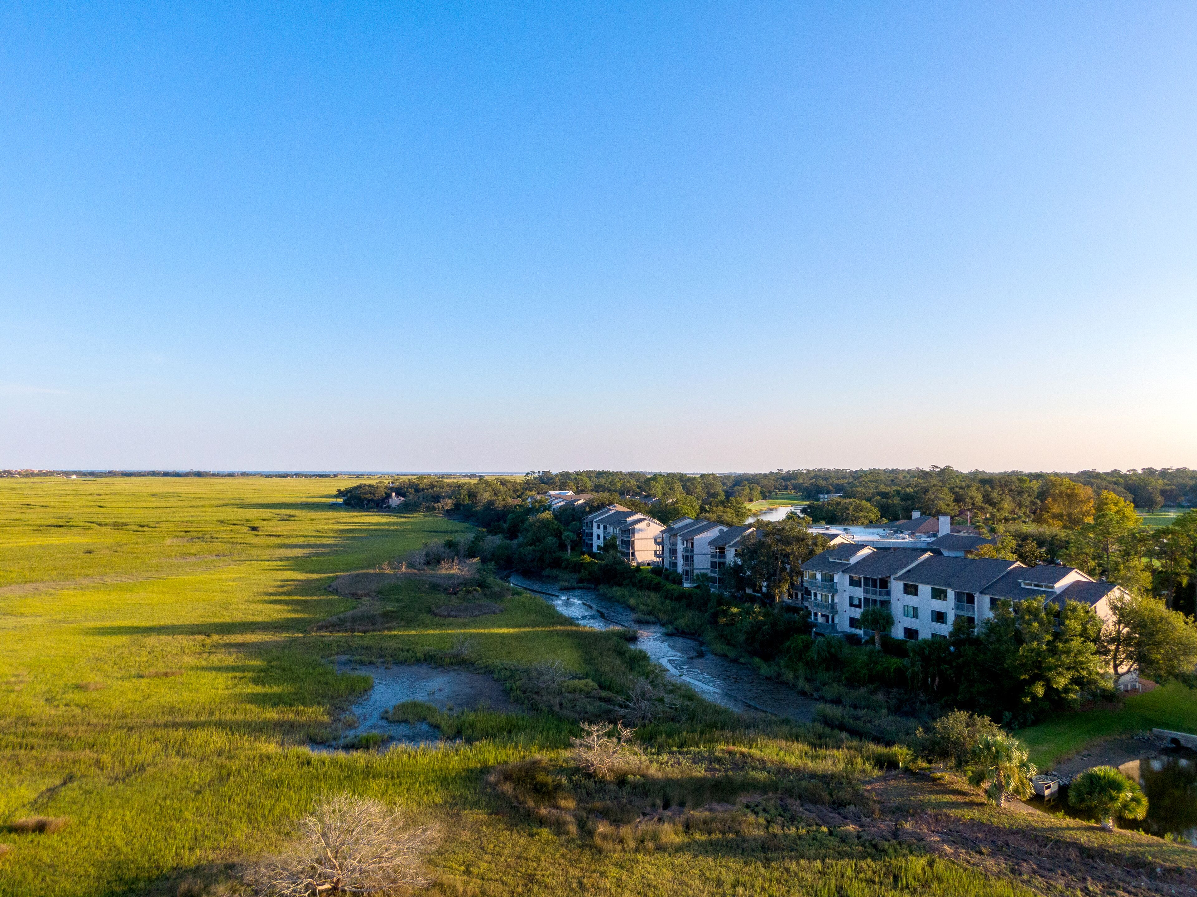 A residential area with modern multi-story buildings, a river, and open green fields.
