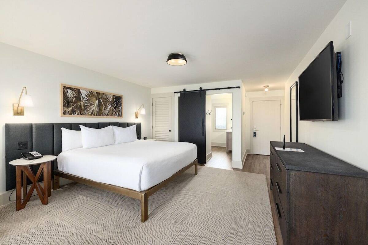 Habitación de hotel con cama, mesita de noche, lámpara, obra de arte, televisor y armario.