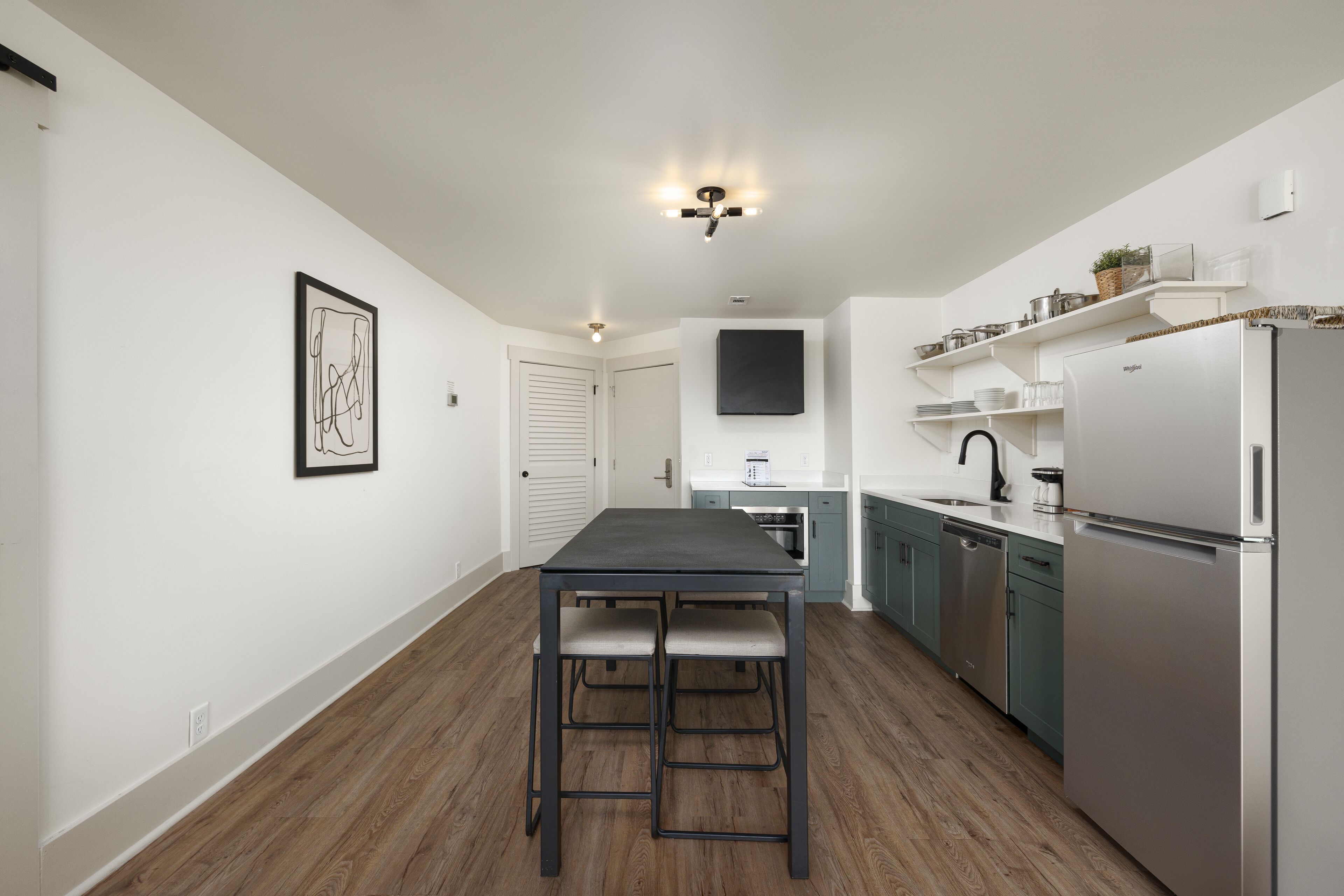 Una cucina moderna con pavimento in legno, pareti bianche e un frigorifero in acciaio inossidabile.
