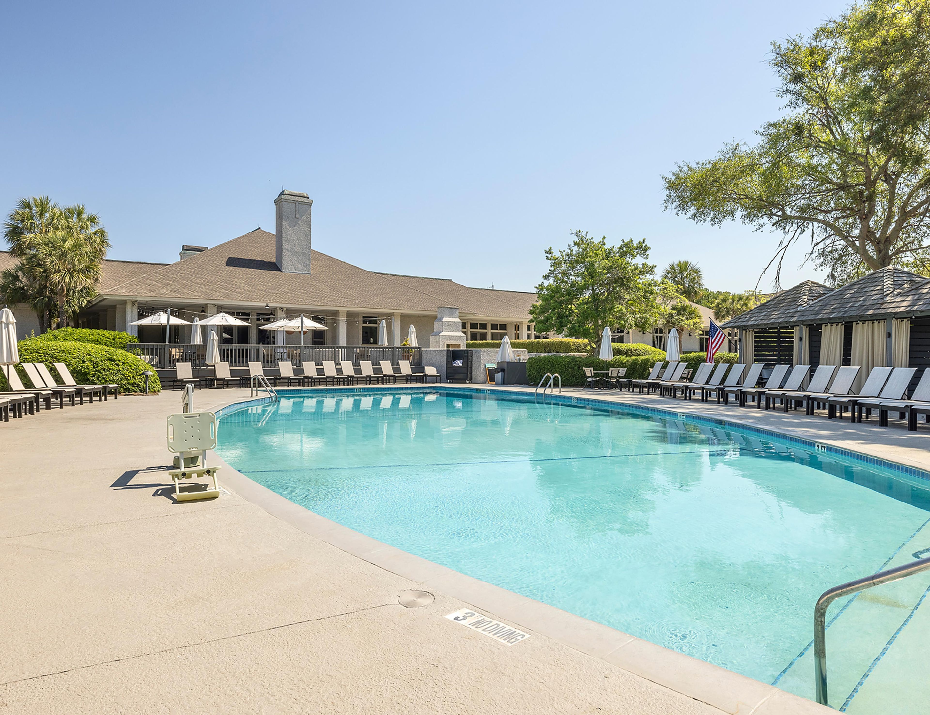 A swimming pool with lounge chairs and umbrellas, a building with a chimney, and a clear sky.