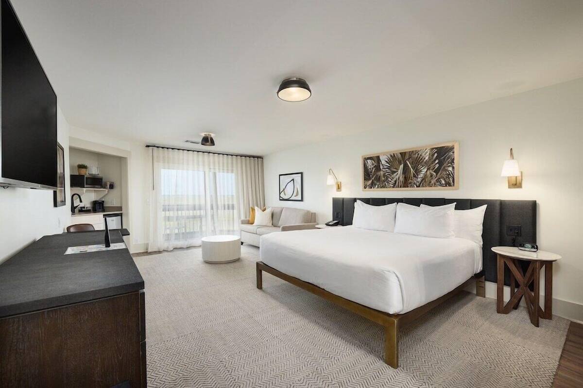 Habitación de hotel con una cama grande, un escritorio, una silla, una mesita pequeña y un televisor.