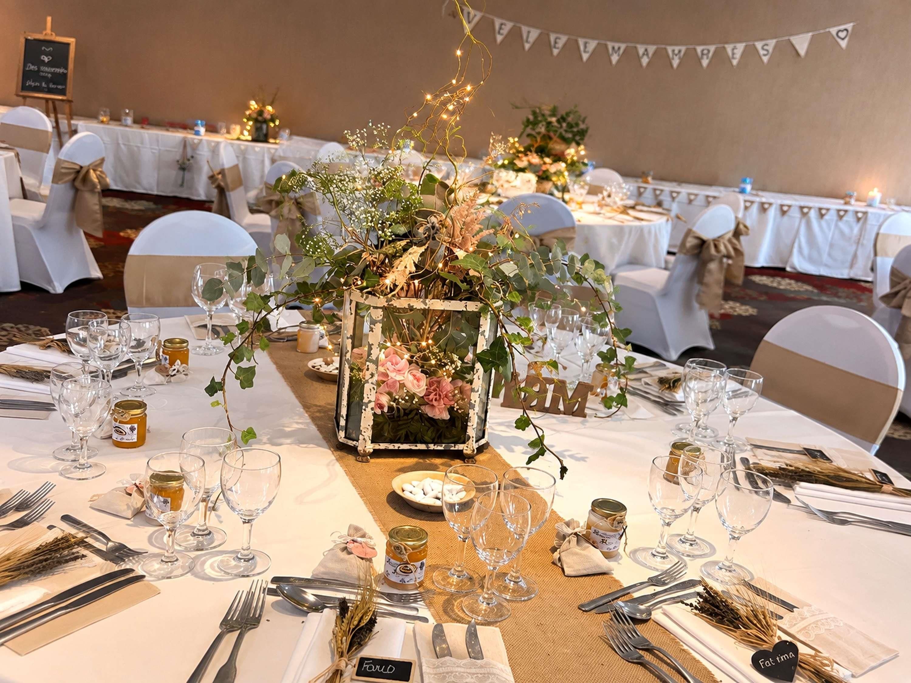 A banquet table set with glassware, plates, and cutlery, surrounded by chairs with white covers and gold sashes.