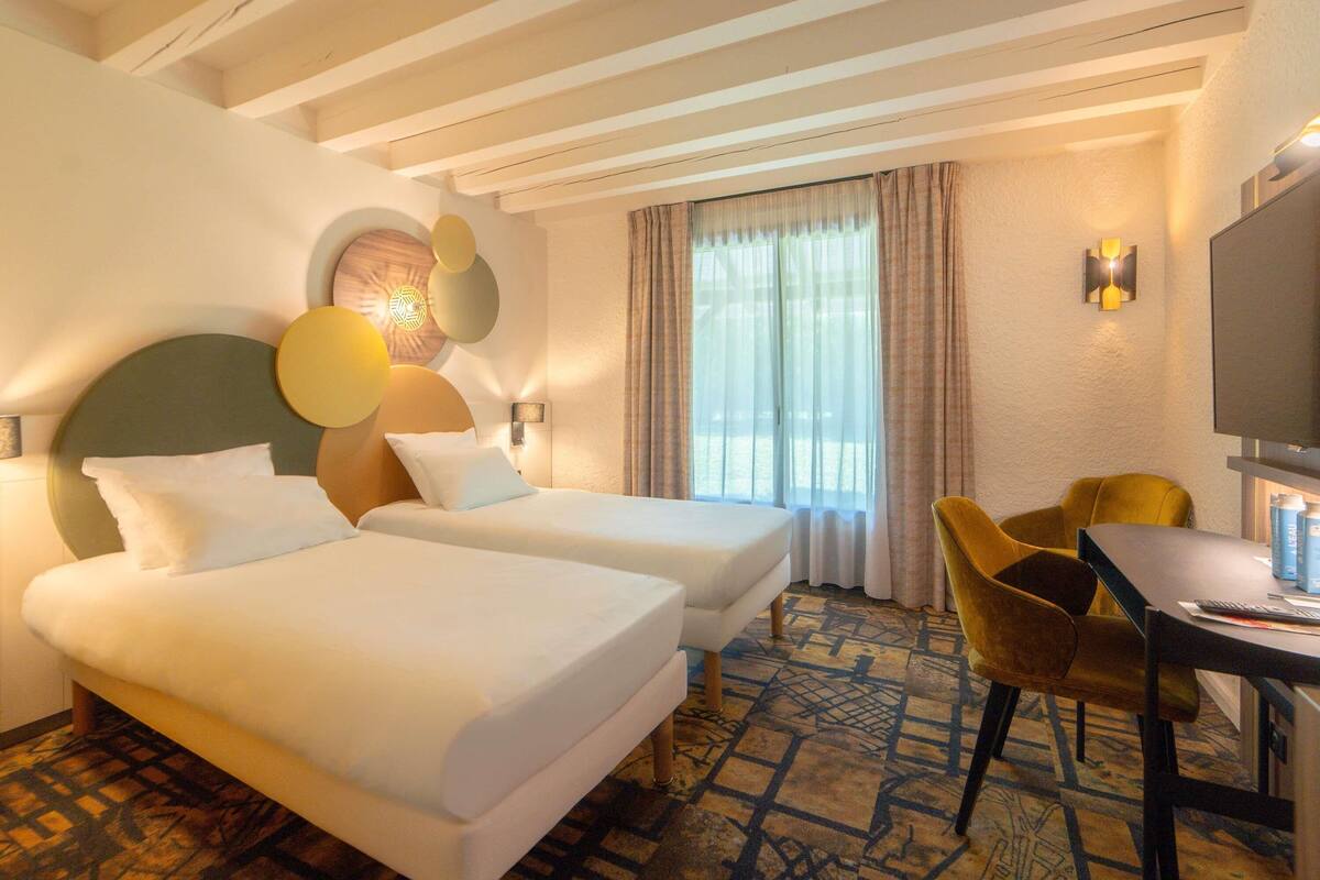 Ein Hotelzimmer mit zwei Betten, einem Schreibtisch und einem Fernseher.