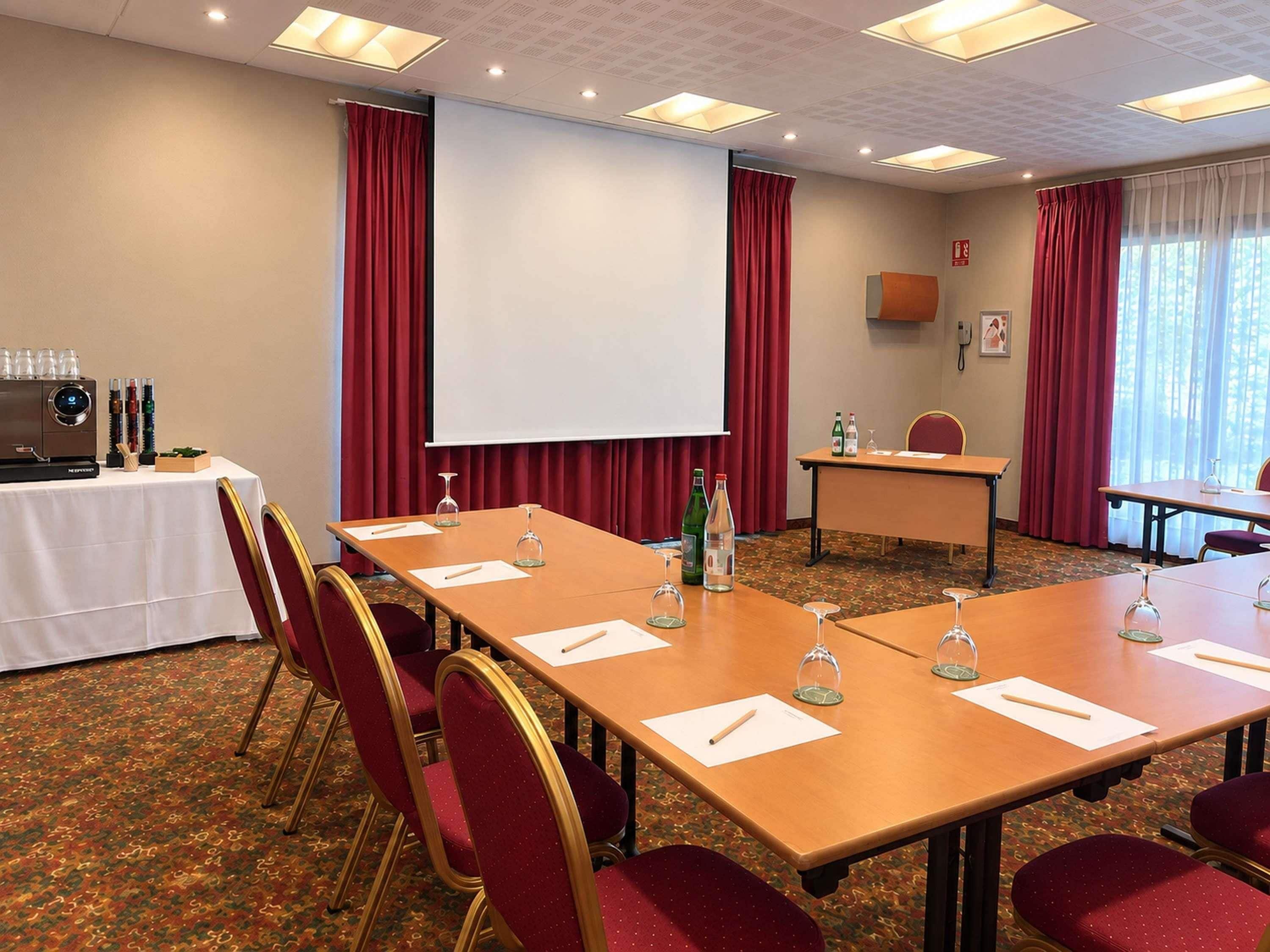 A conference room with a long table, red chairs, a projector screen, and a coffee station.