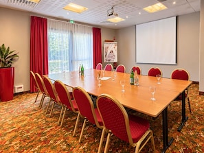 A conference room with a long table, red chairs, a projector screen, and a large window with curtains. - Mercure Auxerre Autoroute du Soleil (Appoigny)