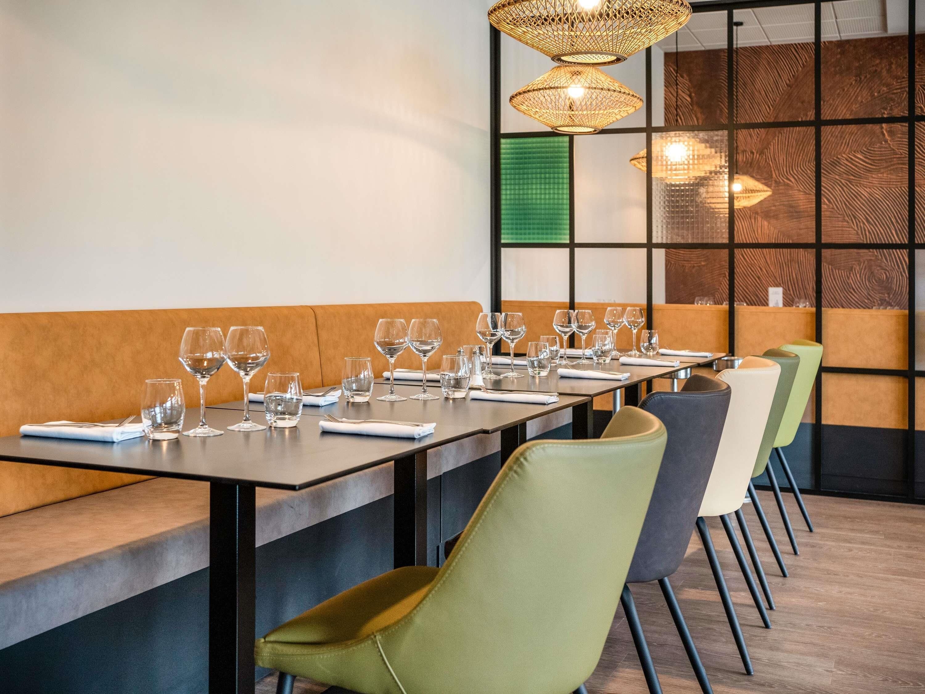 A restaurant interior with a long dining table, multiple chairs, and hanging pendant lights.