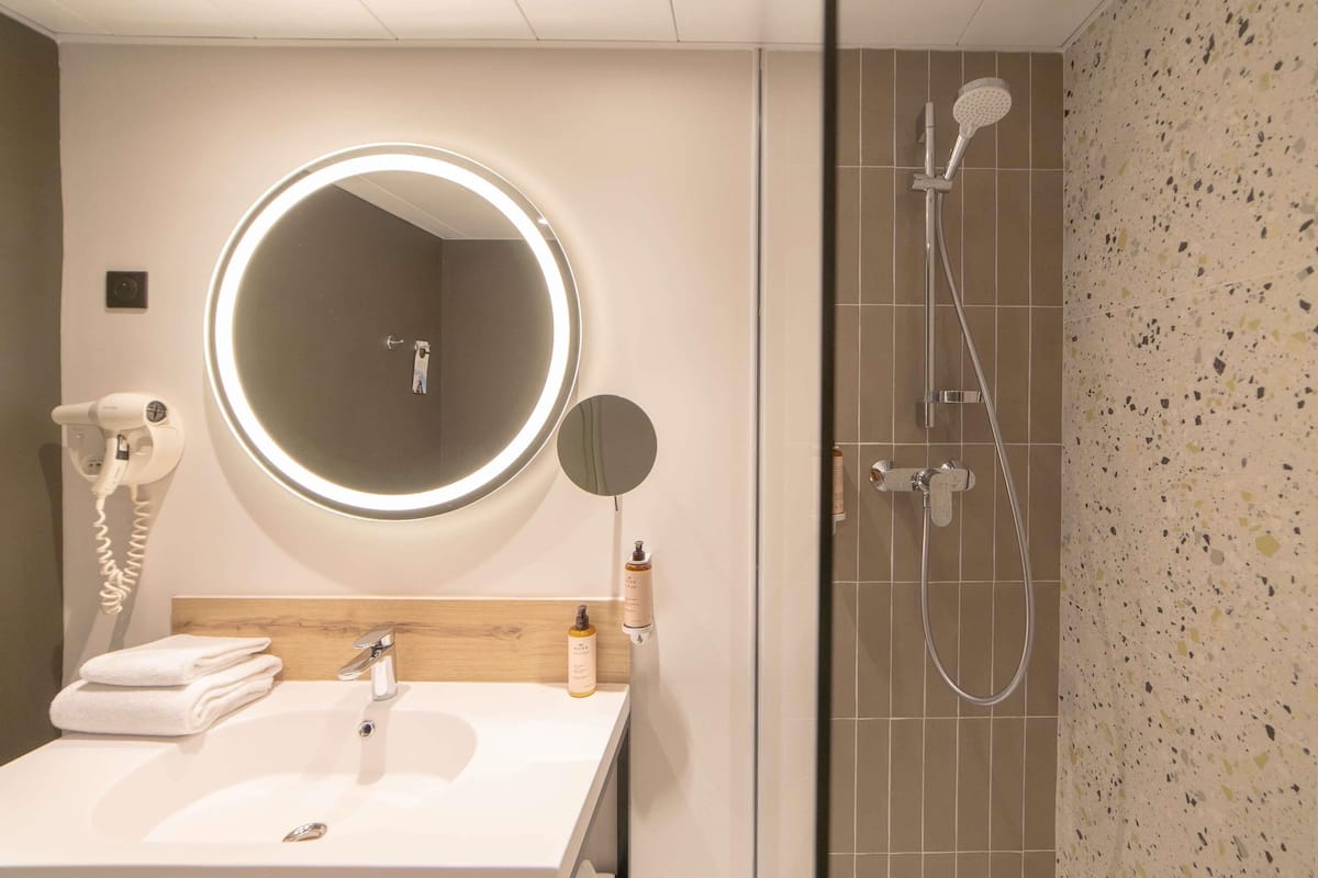 A bathroom with a round mirror, a hairdryer, a sink, and a shower.