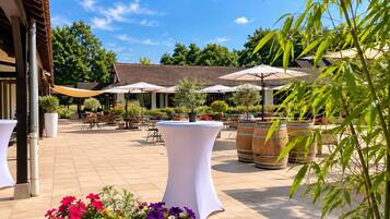 Un espace extérieur aménagé en terrasse, avec des tables et des chaises, entouré de plantes en pot et agrémenté de parasols.