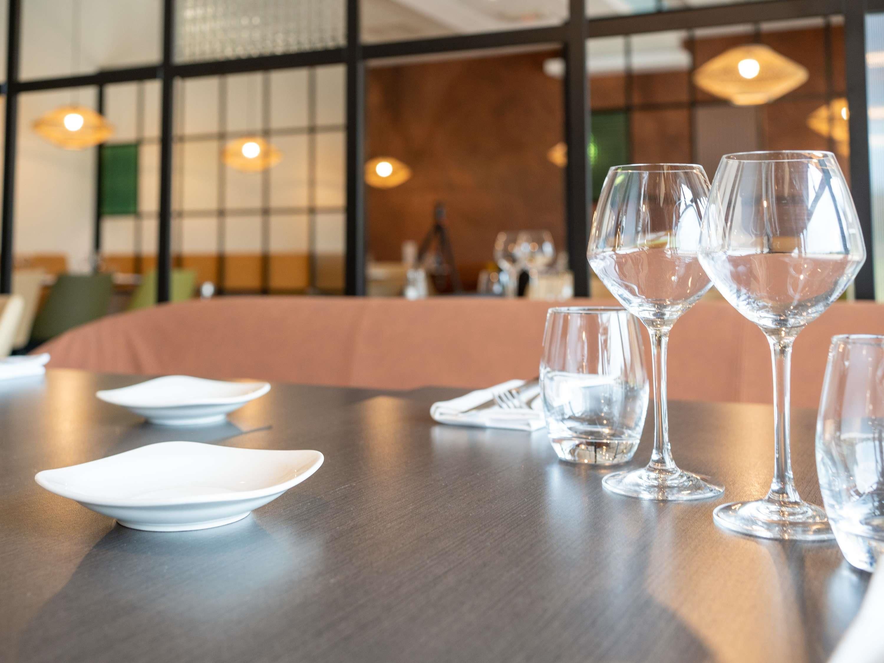 A dining table with clear glassware and plates, a wooden table, and a cushioned bench in a restaurant setting.
