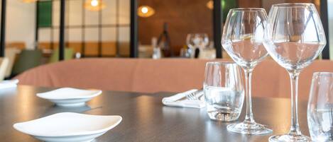 A dining table with clear glassware and plates, a wooden table, and a cushioned bench in a restaurant setting.