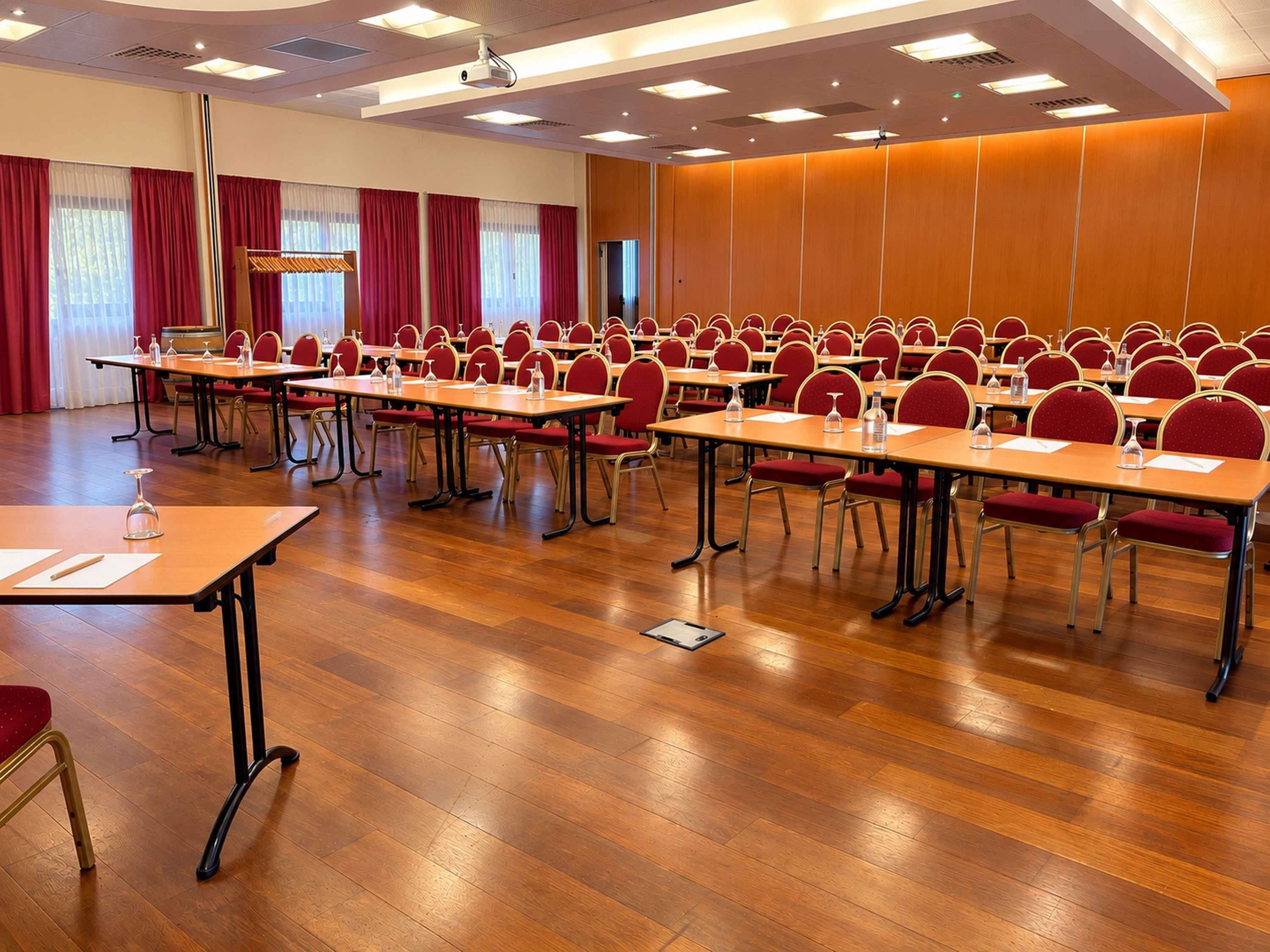 A conference room with rows of tables and chairs, equipped with water bottles and glasses.