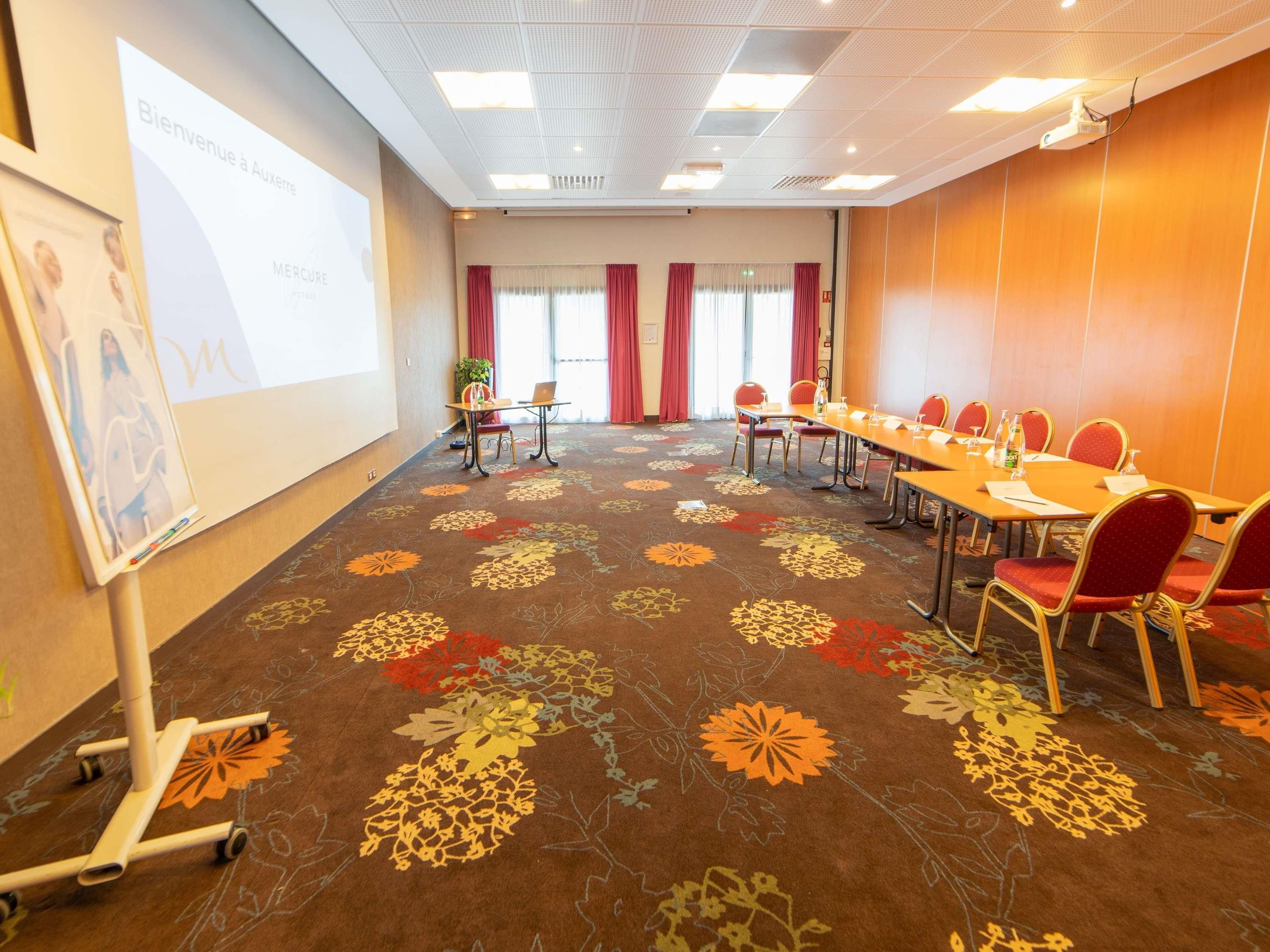 A conference room with a carpeted floor, a projector screen, a whiteboard, and a long table with chairs.