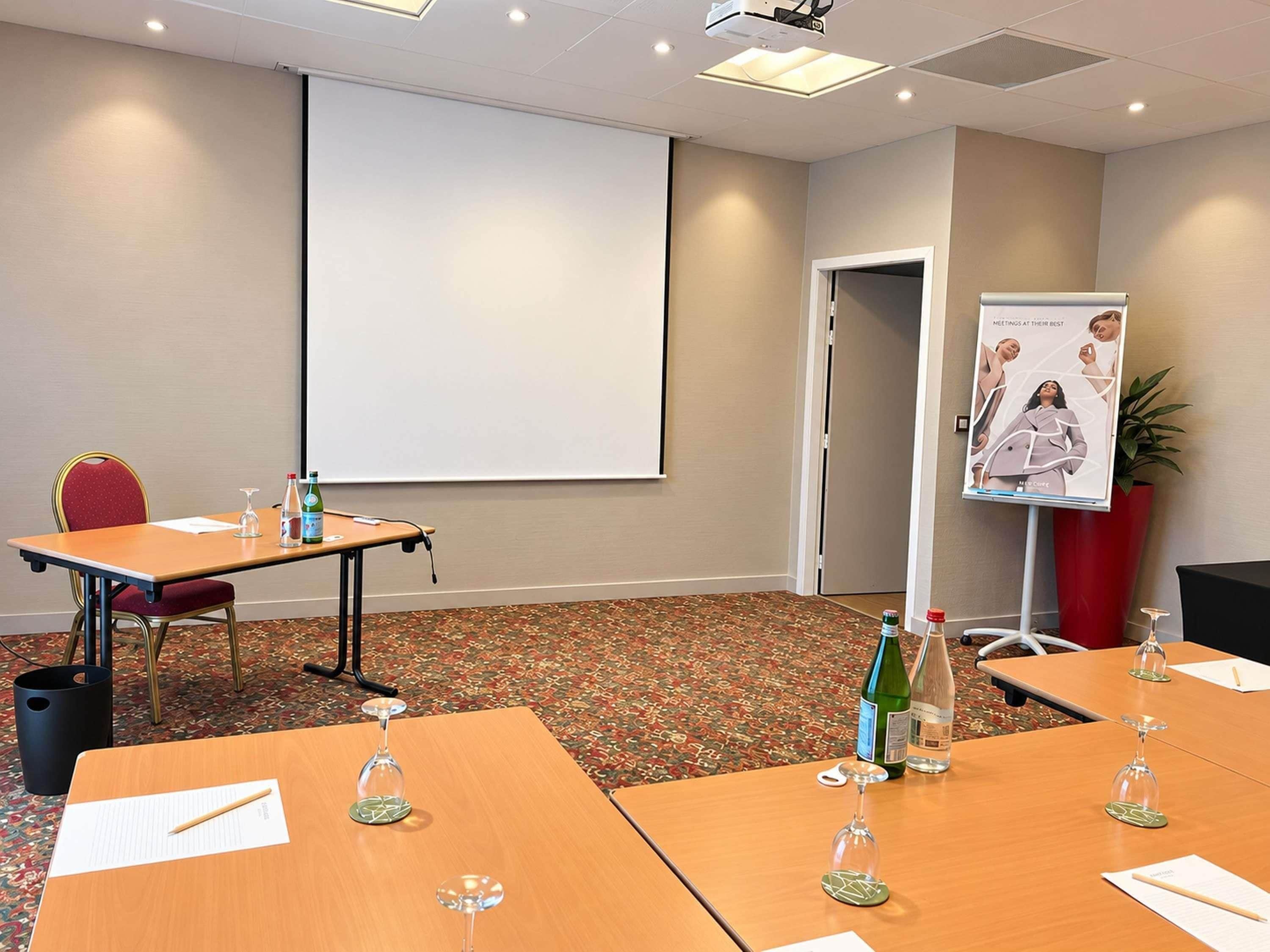 A conference room with a projector screen, a poster, and tables with wine glasses and water bottles.