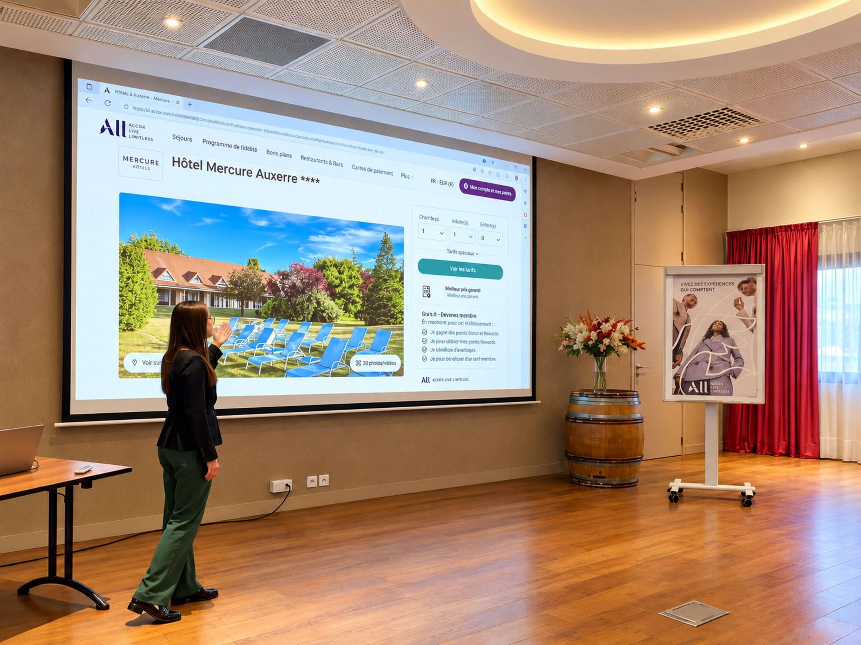 Un écran de présentation affichant la page d’accueil d’un site web d’hôtel, avec une vue de la façade de l’hôtel, une interface de réservation et une affiche promotionnelle.