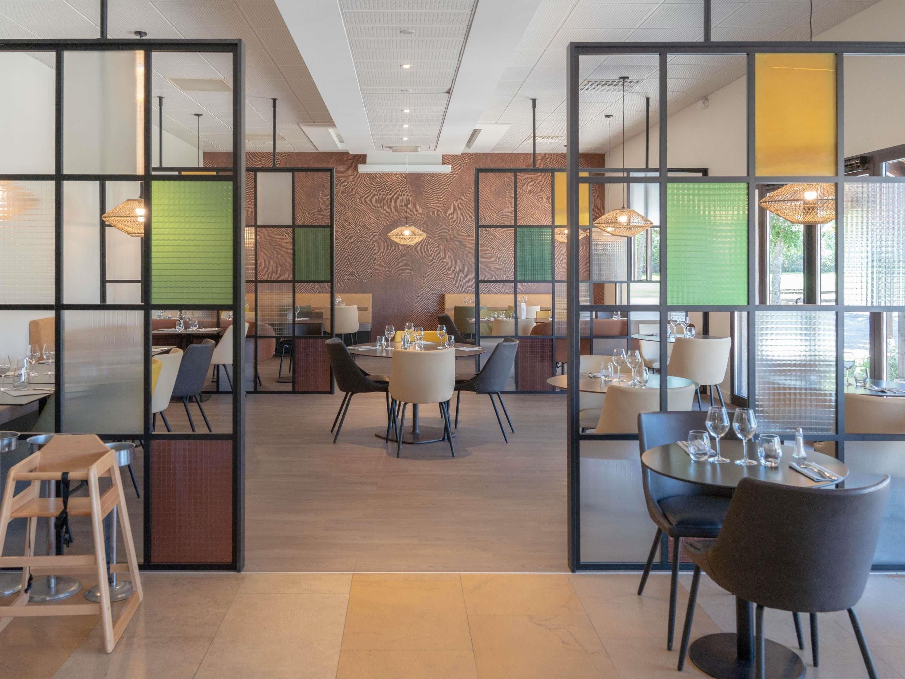 Un comedor moderno con mesas dispuestas para comidas, un área de estar central y vistas a través de un separador.