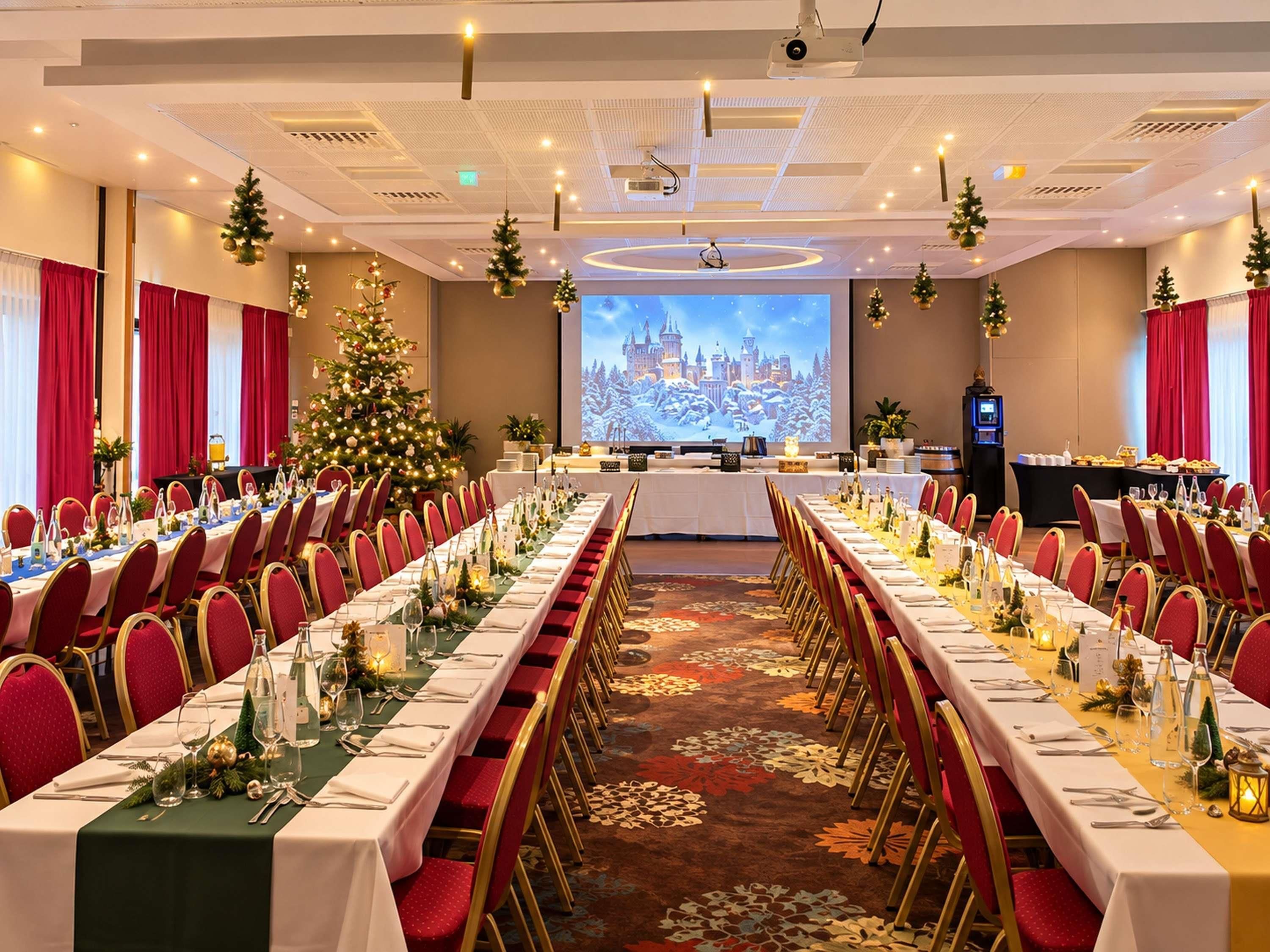Ein Konferenzraum mit langen Tischen, der für eine festliche Veranstaltung hergerichtet ist, dekoriert mit Weihnachtsbäumen und einer großen Leinwand, die eine verschneite Schlosslandschaft zeigt.