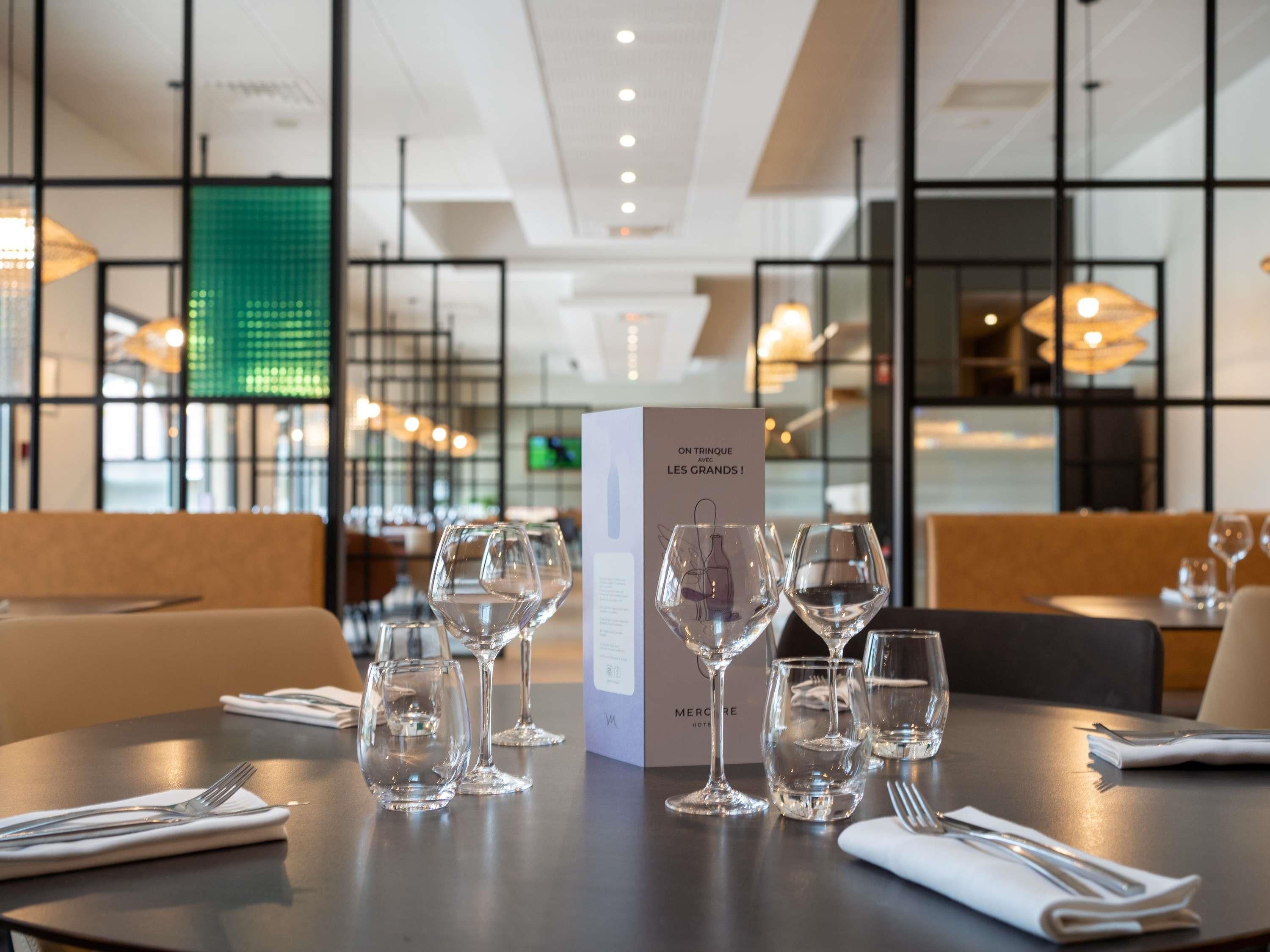 Une table de restaurant mise avec des verres à vin, un présentoir à menus et des couverts.