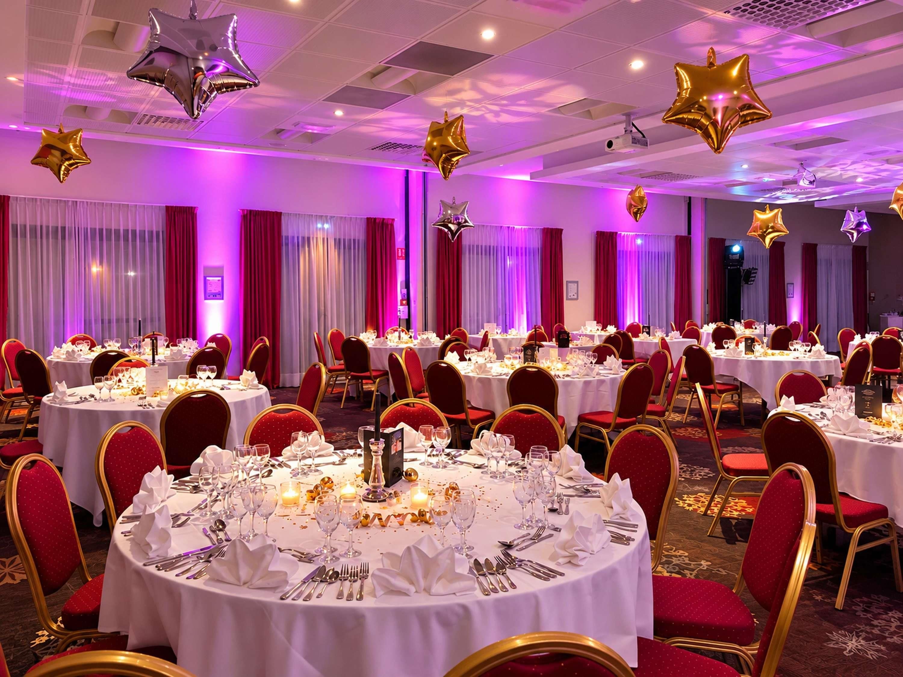 A banquet hall with round tables, red chairs, and star-shaped decorations.