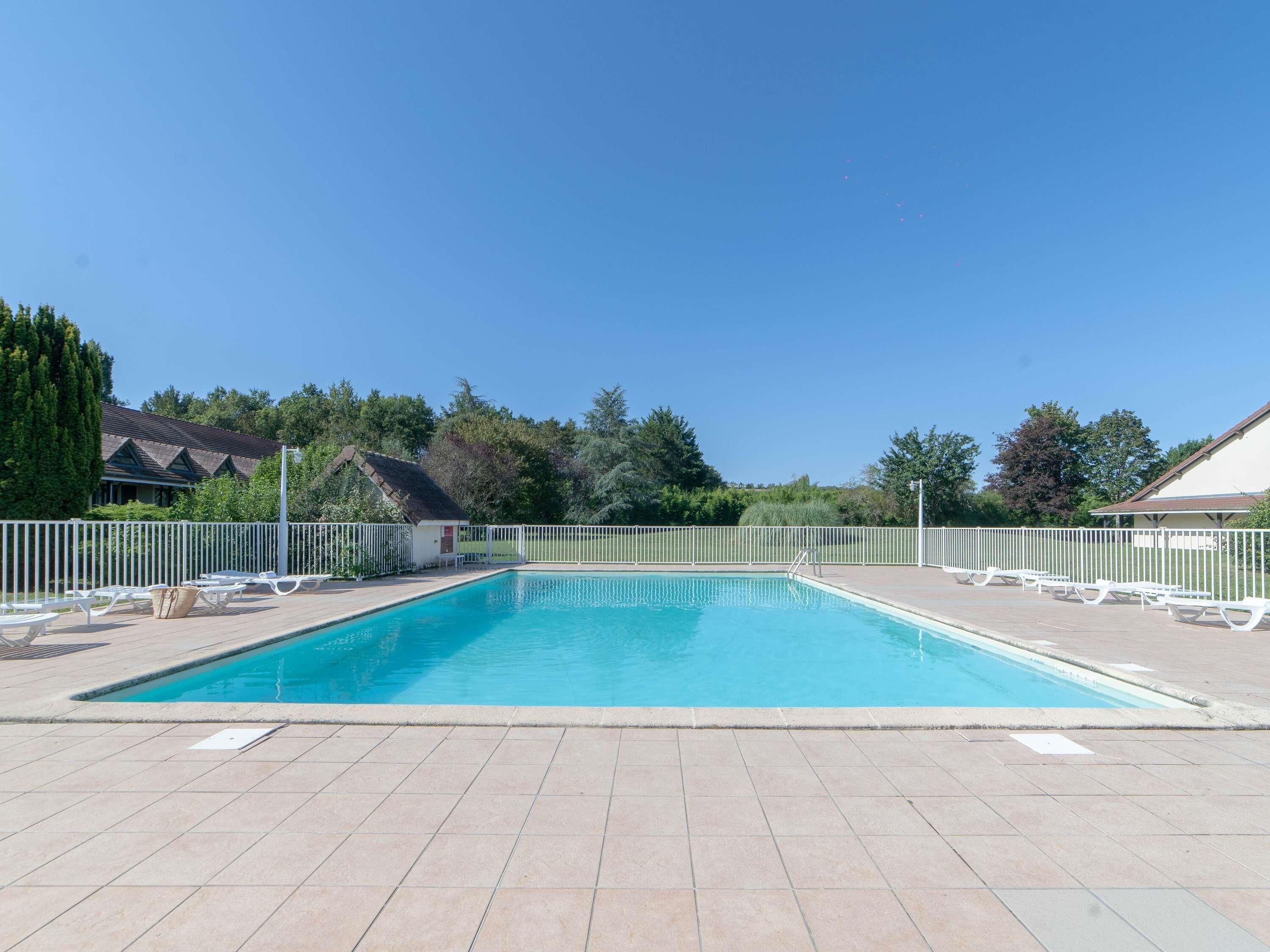 Piscina rectangular con plataforma de azulejos, rodeada de barandillas blancas y sillas de descanso.
