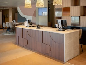 A modern reception desk with a computer, phone, and glass display. There are wooden paneling and a large abstract wall art piece in the background.
