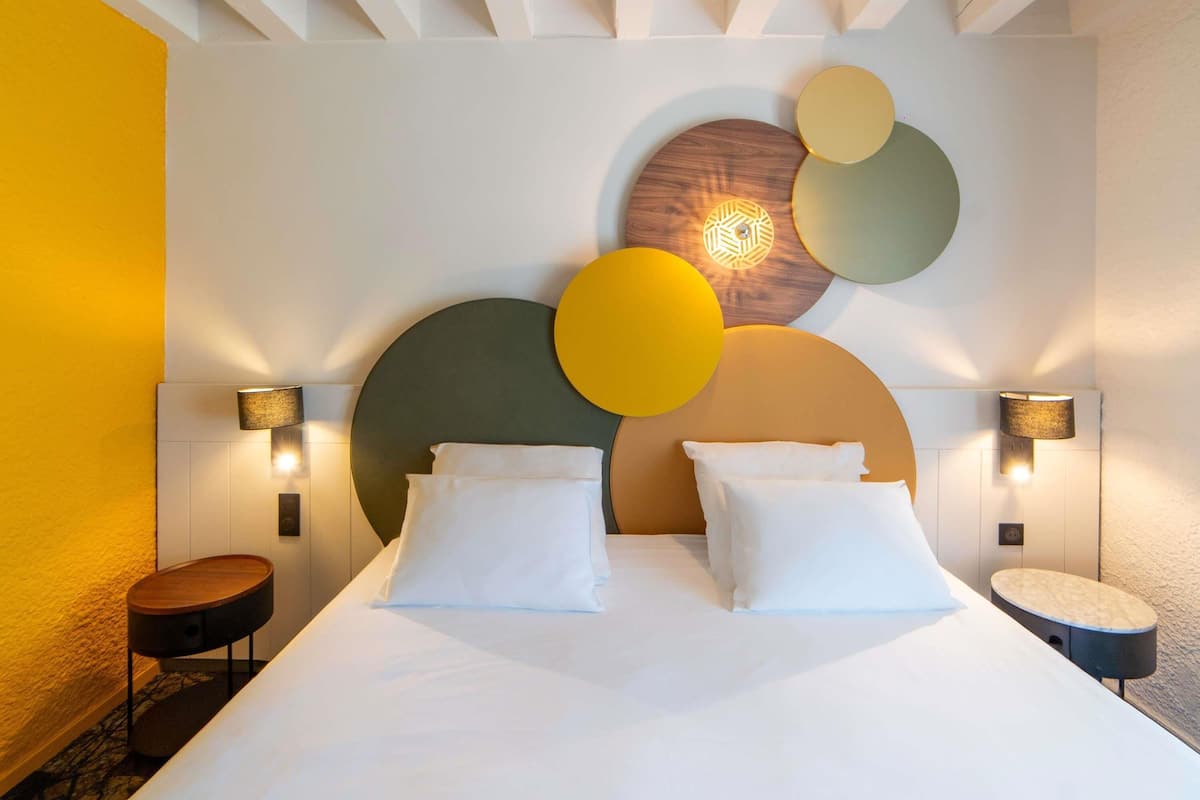 Ein modernes Hotelzimmer mit einem großen Bett, zwei Nachttischen und einem einzigartigen Wandkunstwerk.