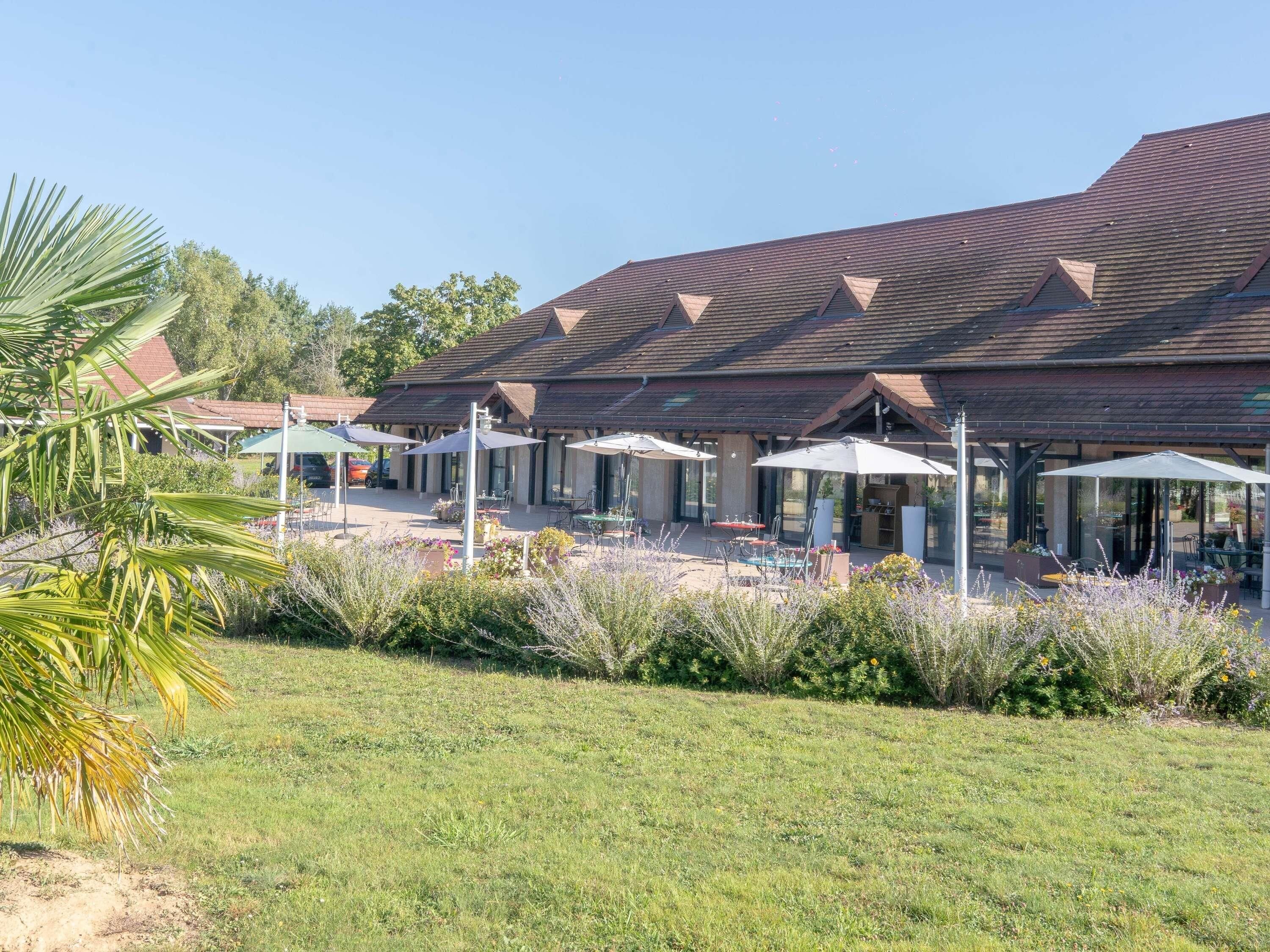 Un bâtiment doté d’un toit en pente et de plusieurs espaces extérieurs aménagés avec des parasols.