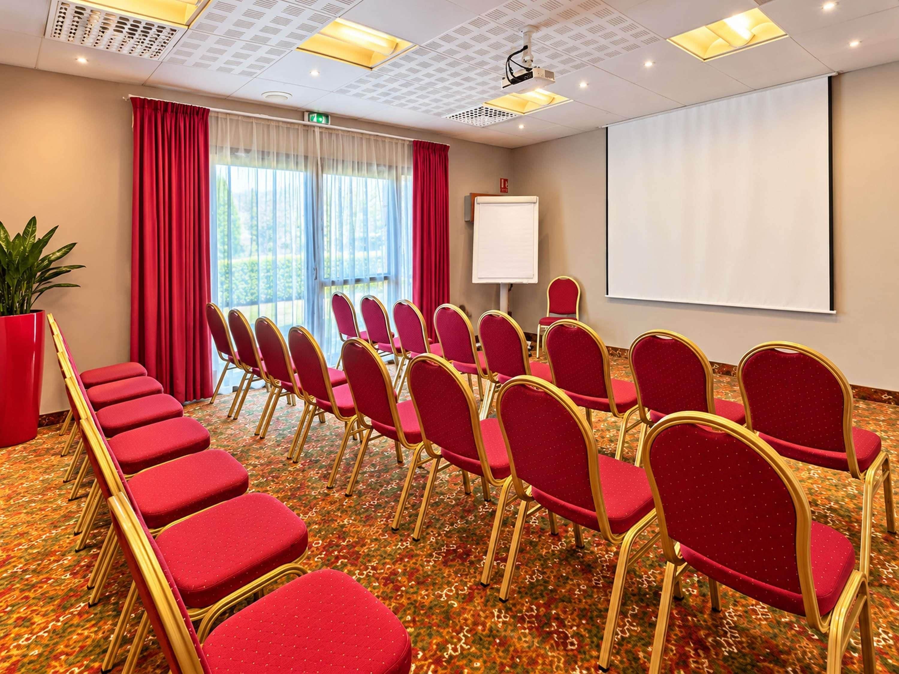 A conference room with rows of red chairs, a whiteboard, and a projector screen.