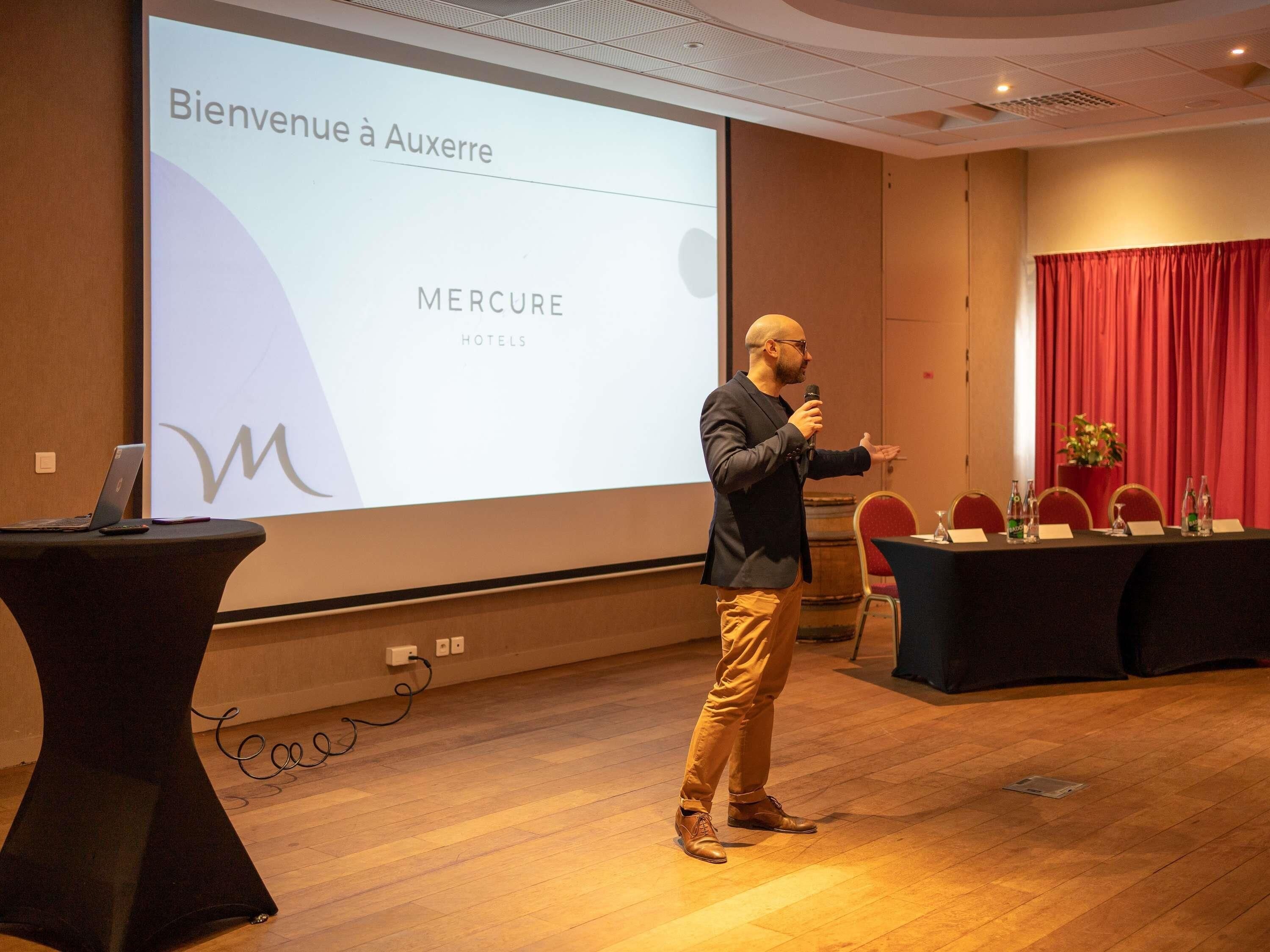 Presentación en una sala de conferencias con una pantalla que muestra 'Bienvenue à Auxerre' y 'MERCURE HOTELS'.